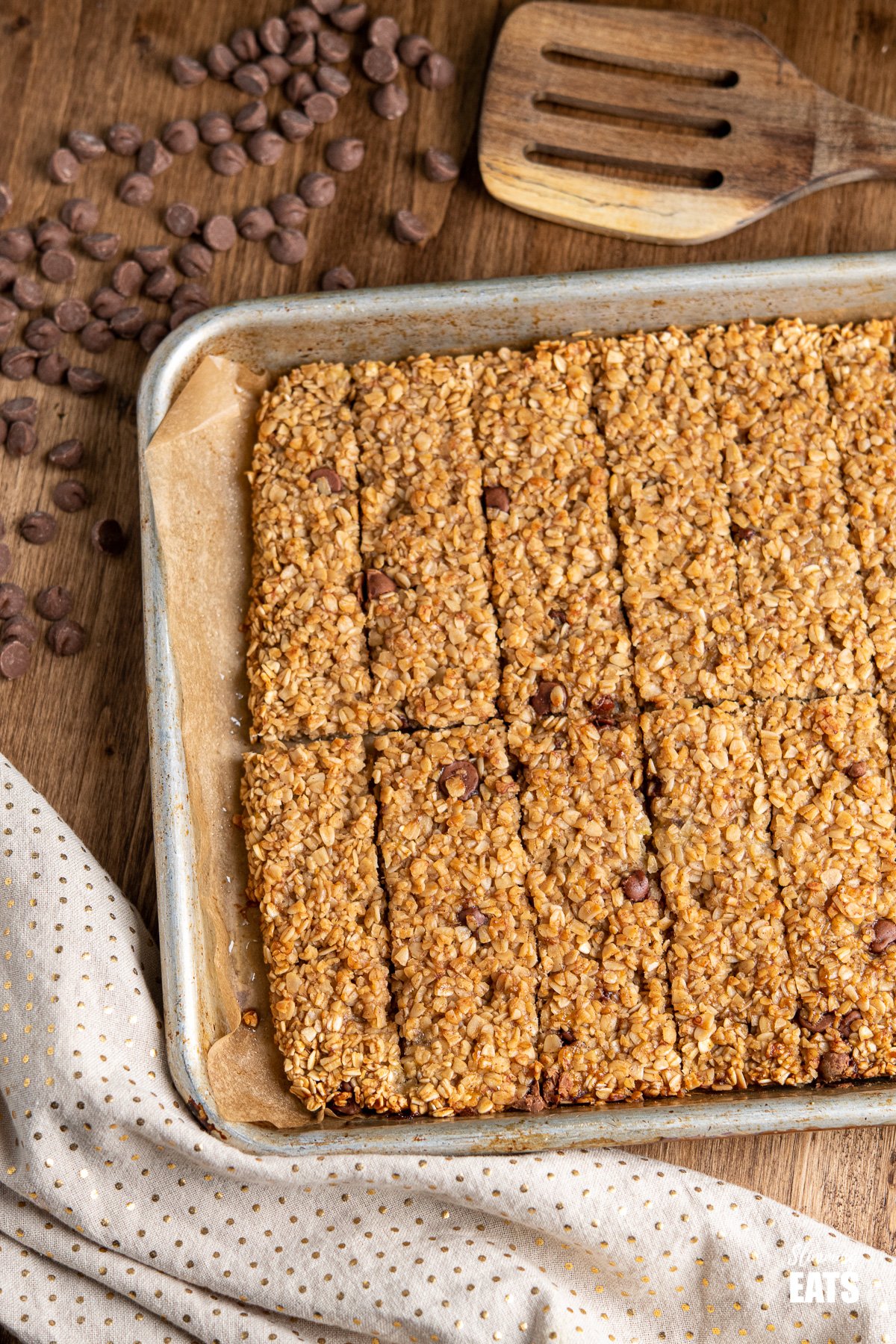 Healthy Chocolate Chip Banana Granola Bars on a baking tray with scattered chocolate chips on wooden board