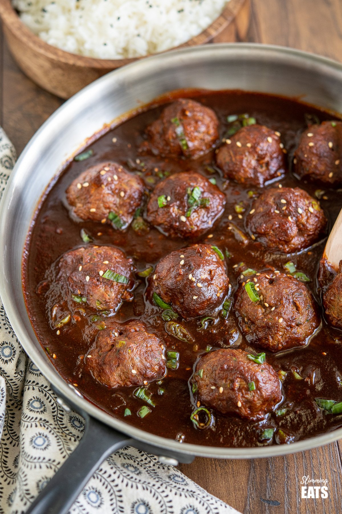 Saucy Asian Hidden Vegetable Beef Meatballs in frying pan with wooden bowl of rice in background