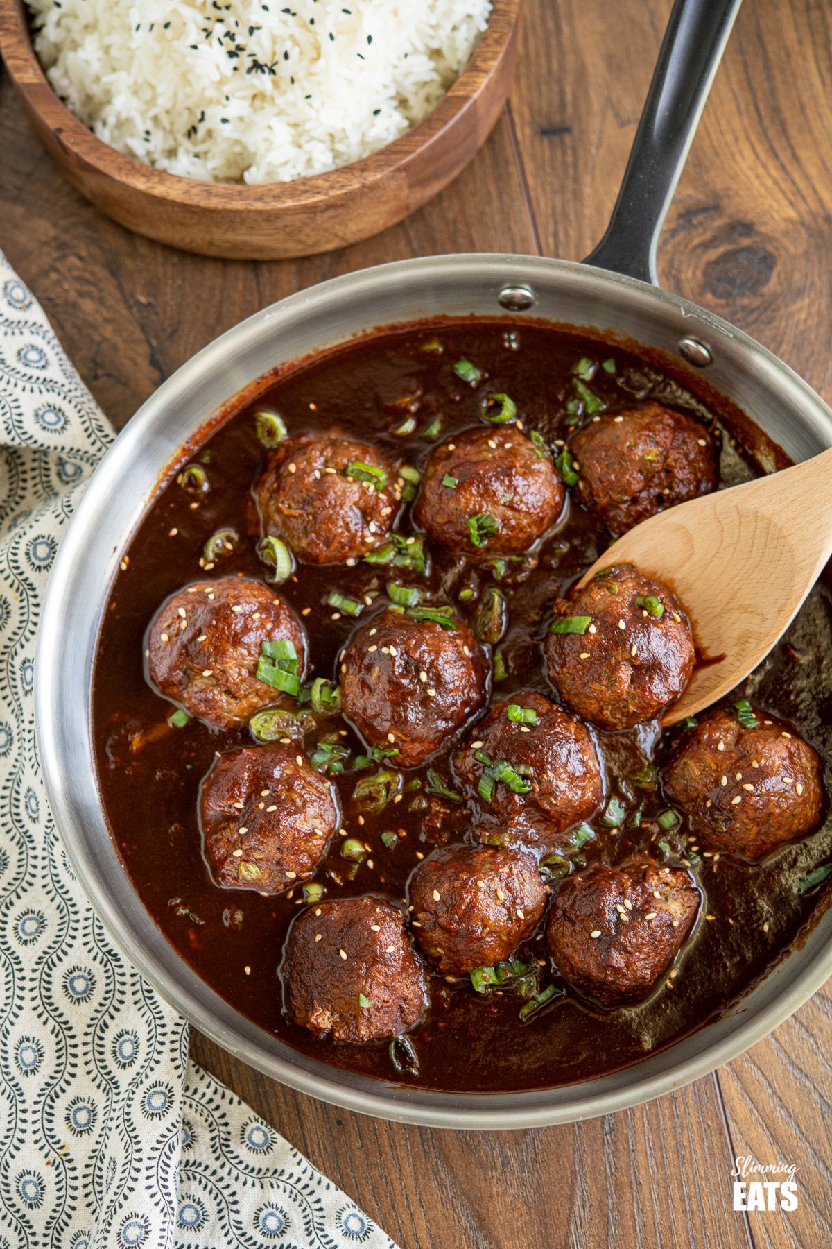 Saucy Asian Hidden Vegetable Beef Meatballs in frying pan with rice in wooden bowl