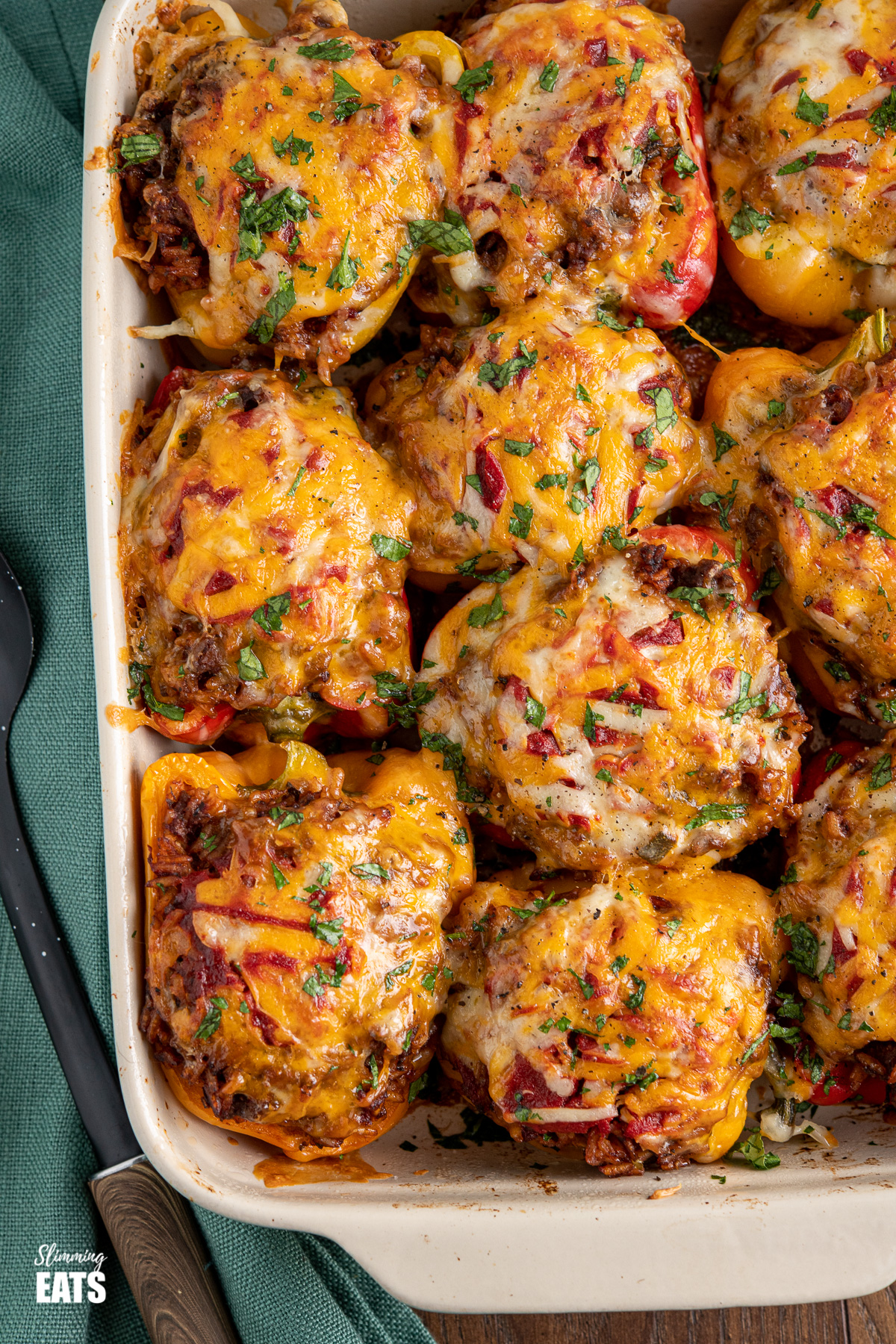 stuffed peppers in baking dish topped with melted golden cheese and chopped parsley, serving spoon placed to the left. 