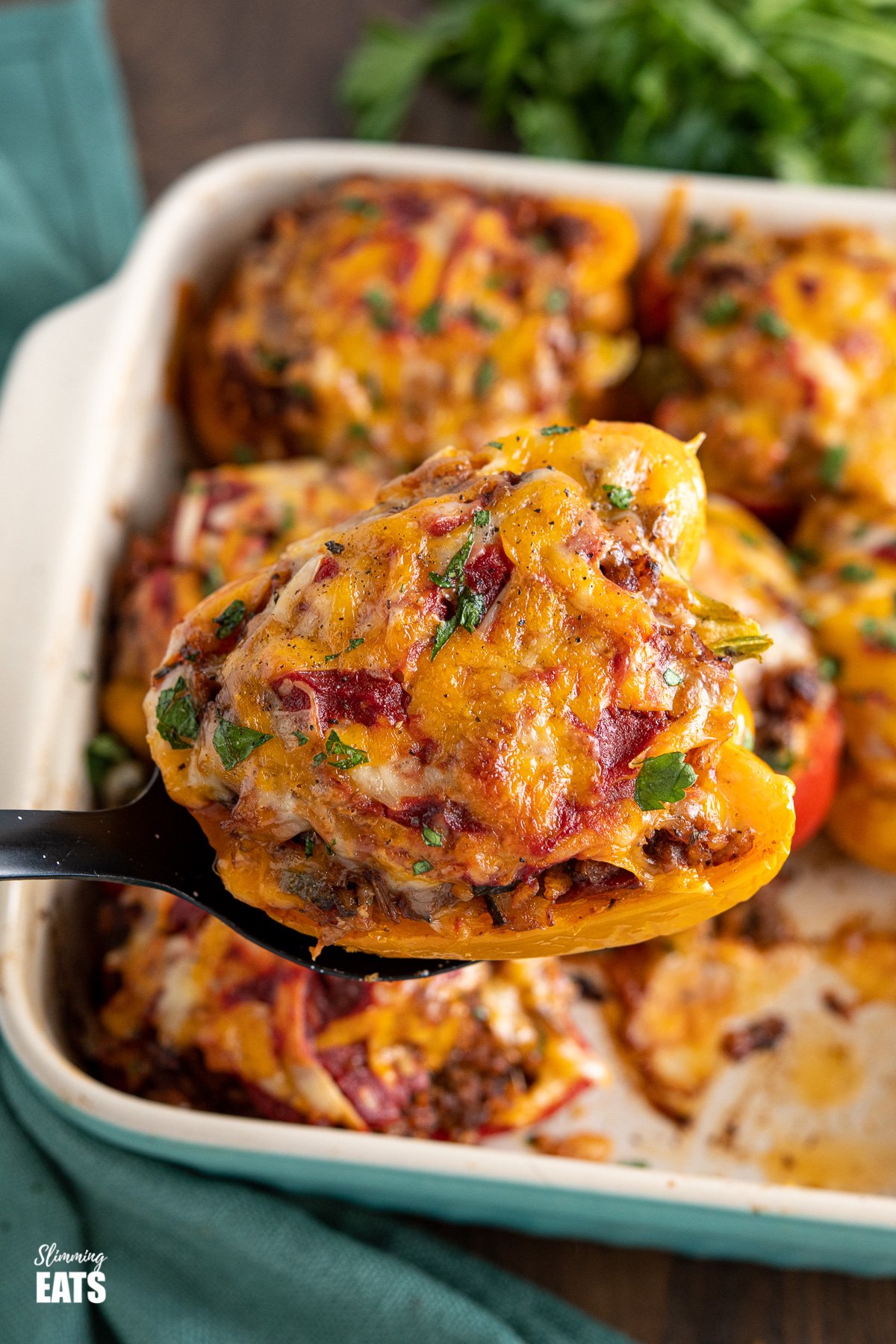 spoon scooping up a stuffed pepper from baking dish, with bunch of parsley in background