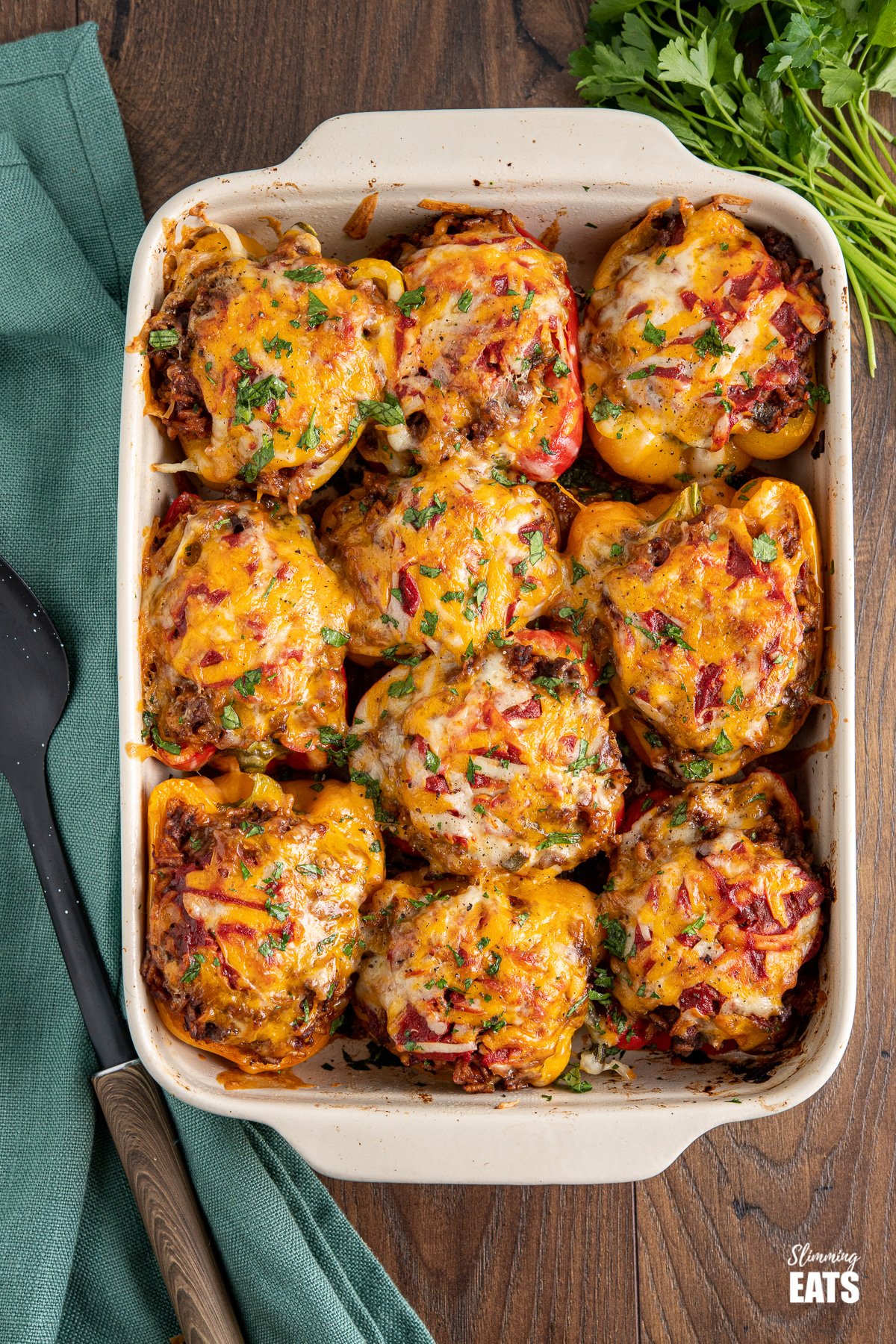 Stuffed Peppers in a baking dish topped with melted cheese on a wooden board with a bunch of parsley