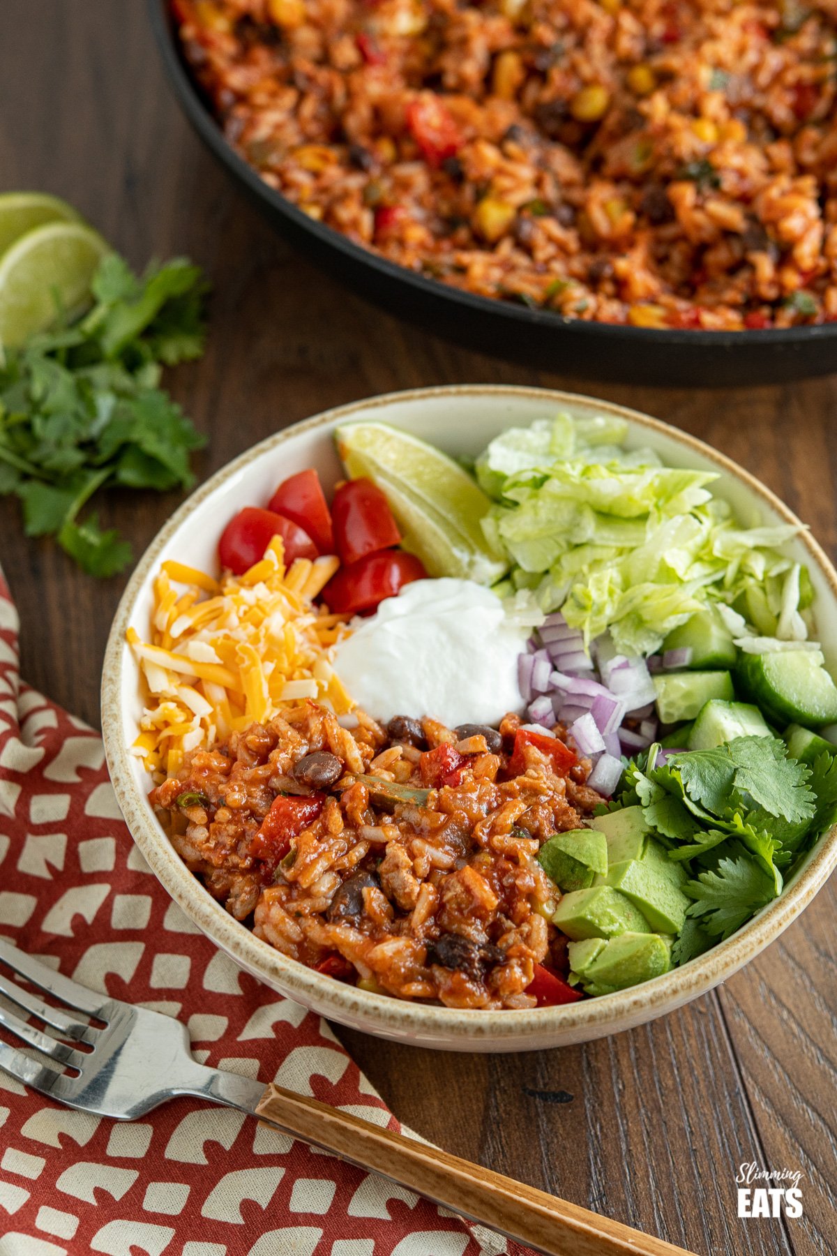 turkey burrito bowls with cheddar, sour cream, tomatoes, lettuce, cilantro and avocado, frying pan with rice in background