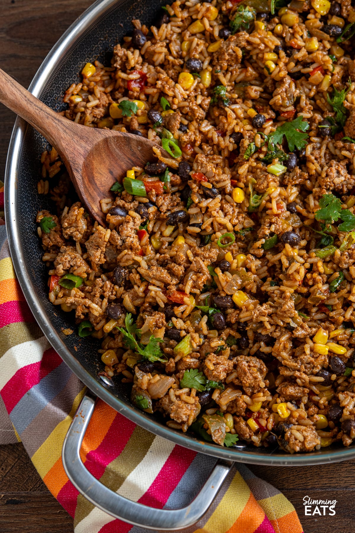 close up of wooden spoon in One Pan Turkey Burrito Rice in a double handled non stick skillet