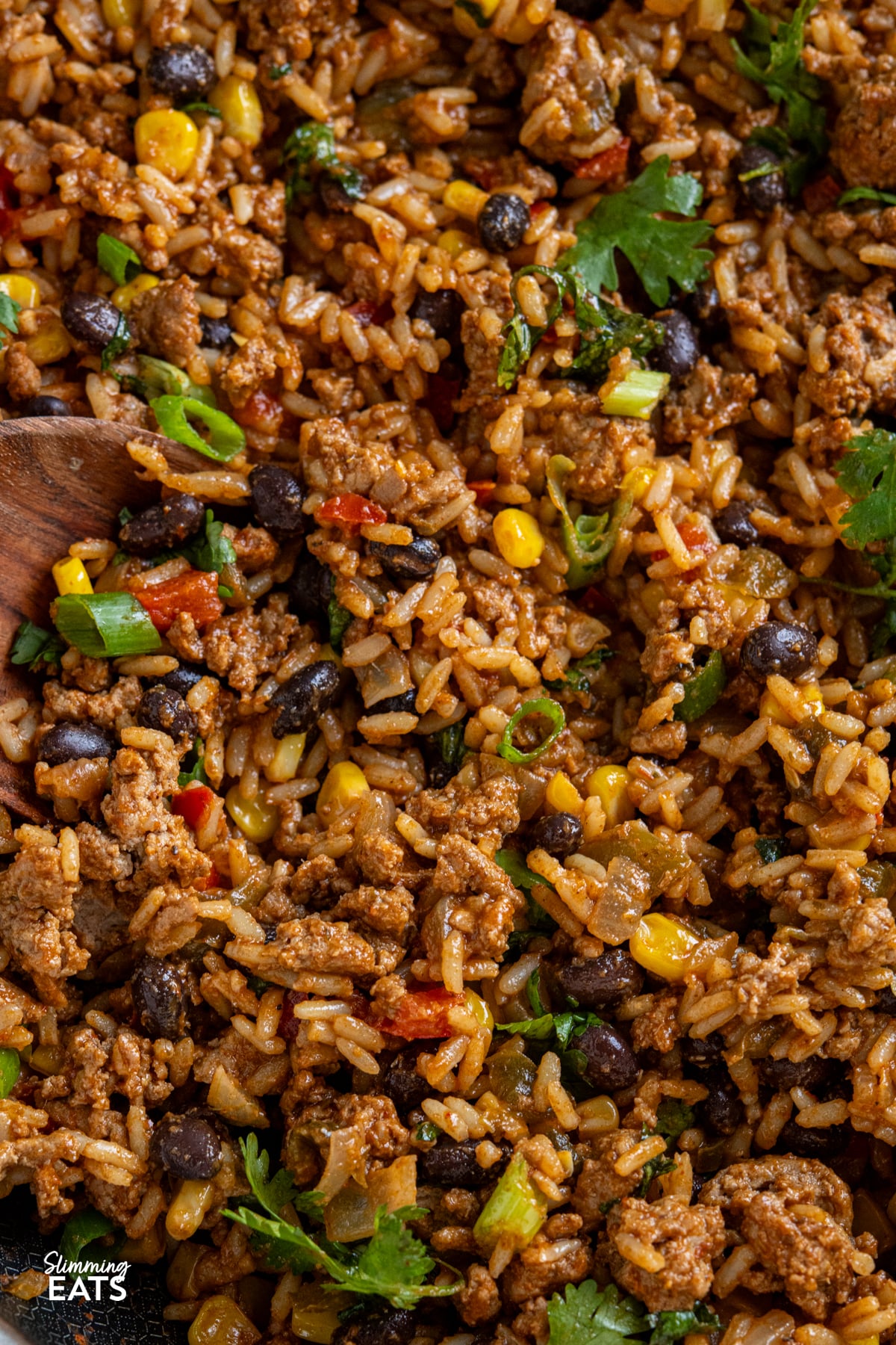These Turkey Rice Burrito Bowls make a great family meal - sit down and grab a bowl with your favourite toppings. Gluten free, dairy free, Slimming Eats and Weight Watchers friendly close up of wooden spoon in One Pan Turkey Burrito Rice in a double handled non stick skillet