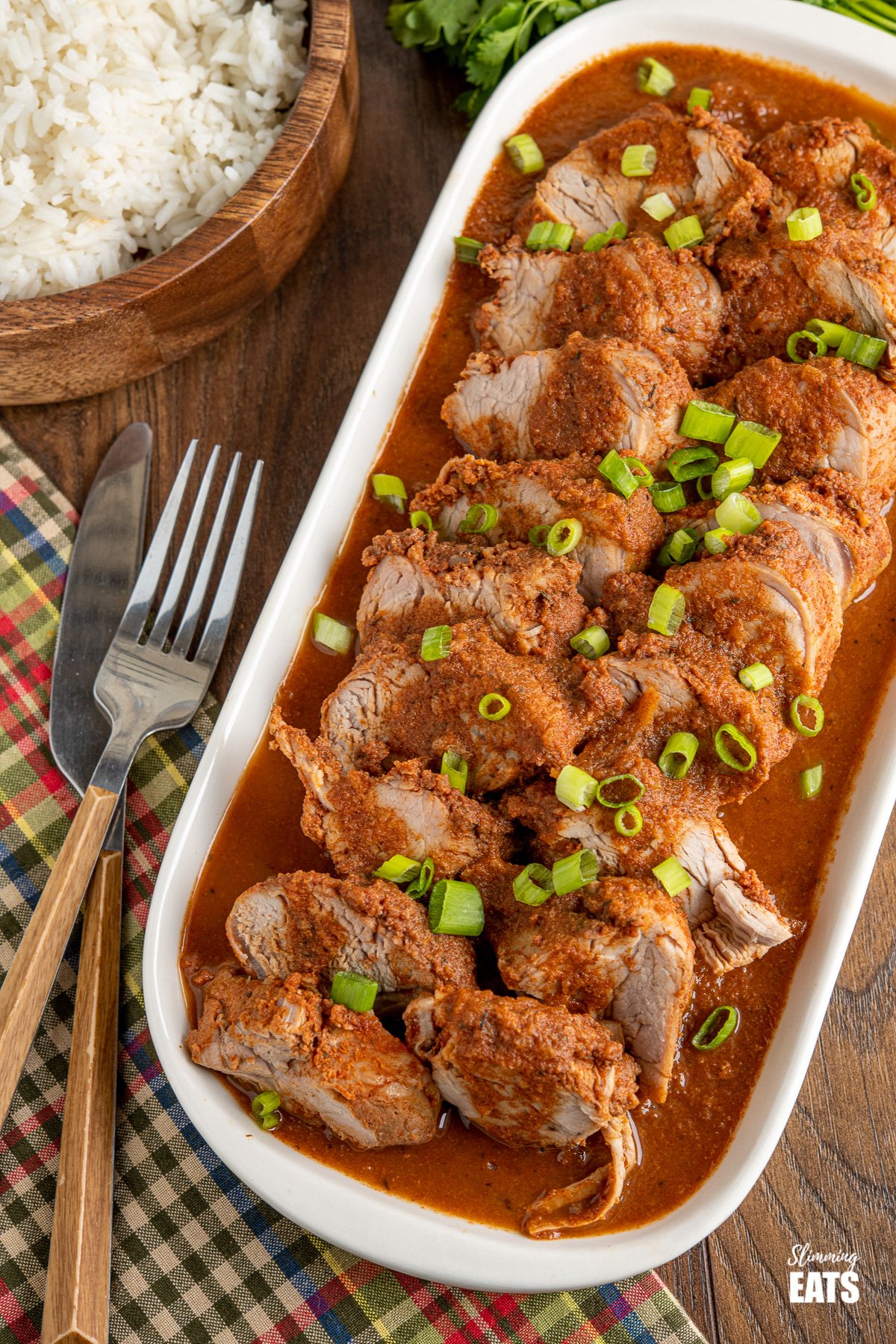 plated up sliced Slow Cooker Cajun Apple Pork Tenderloin with a wooden bowl of rice on th side