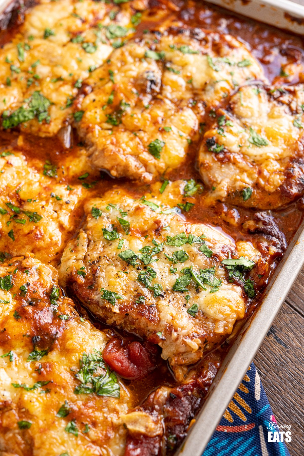Cheesy Topped Mediterranean Pork Loin Chops - tender pork loin chops in a rich mediterranean style sauce topped with cheese and broiled until melted and golden. Gluten Free, Slimming Eats and Weight Watchers friendly close up of Cheesy Topped Mediterranean Pork Loin Chops on baking tray