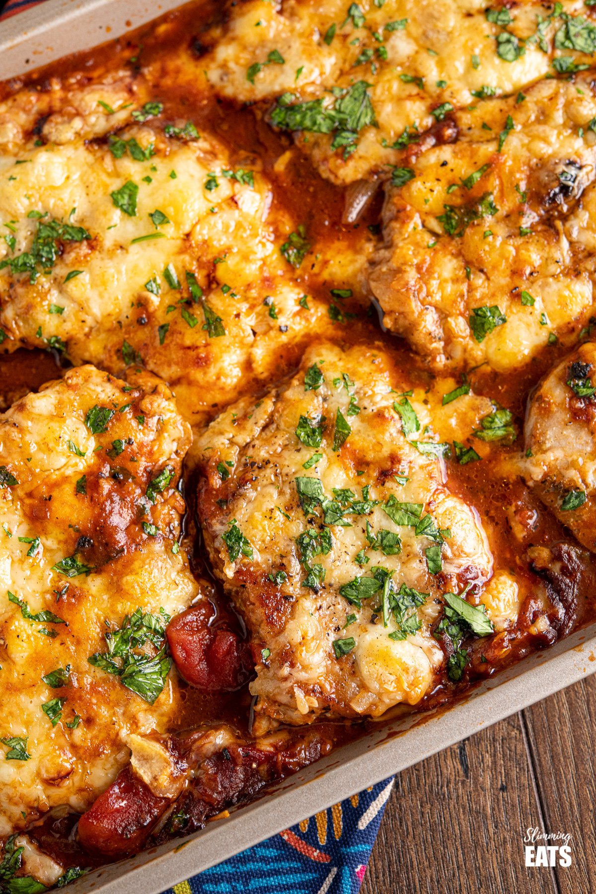 Cheesy Topped Mediterranean Pork Loin Chops - tender pork loin chops in a rich mediterranean style sauce topped with cheese and broiled until melted and golden. Gluten Free, Slimming Eats and Weight Watchers friendly close up of Cheesy Topped Mediterranean Pork Loin Chops on baking tray