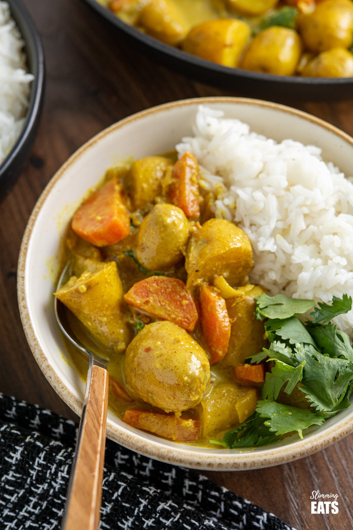 white bowl with beige rim filled with creamy coconut potato curry , rice and cilantro, frying pan in the background