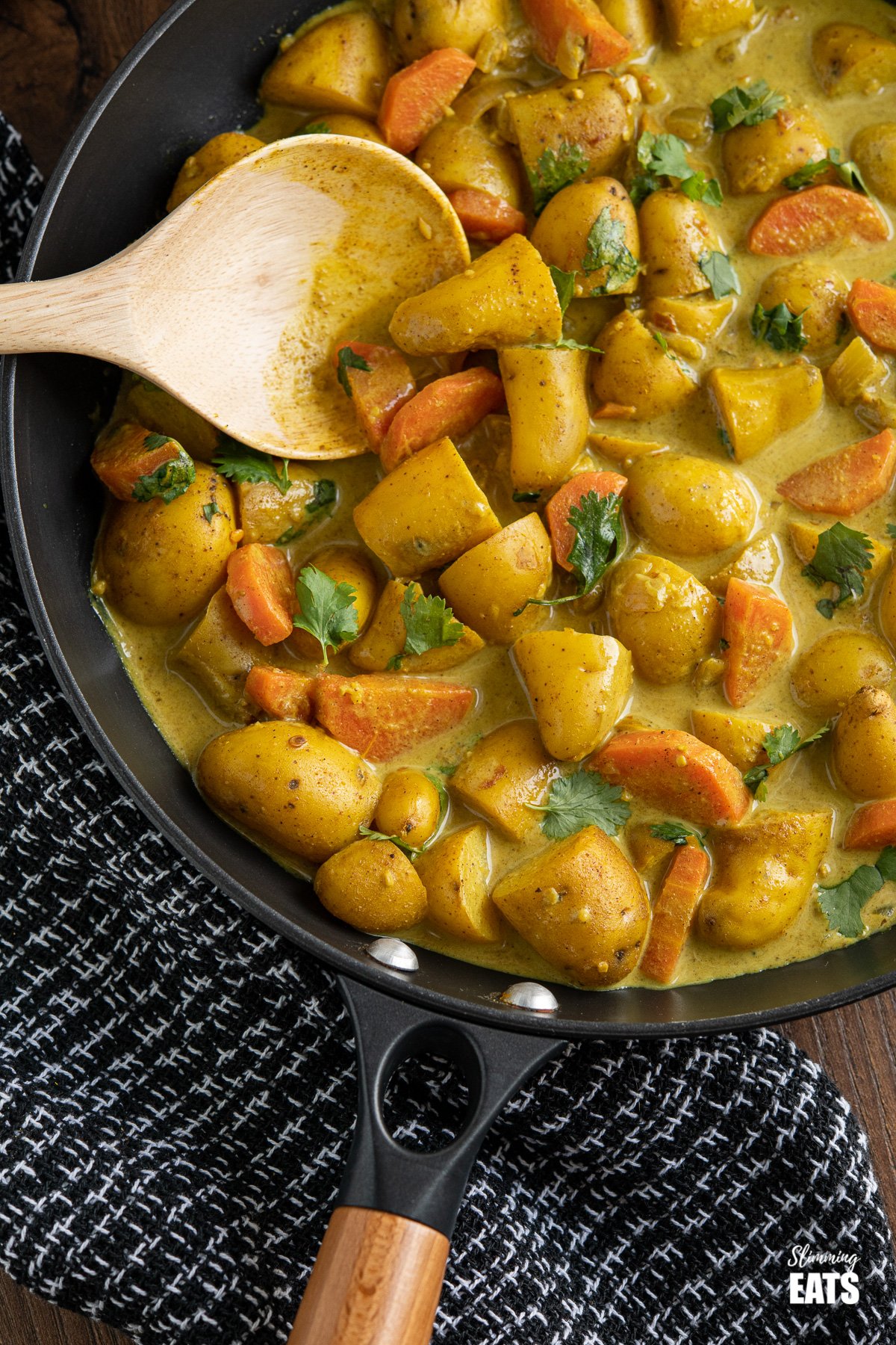 close up of creamy coconut potato curry in black frying pan with wooden handle