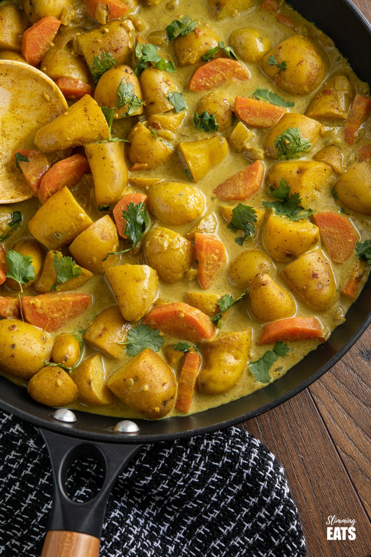 close up of creamy coconut potato curry in back frying pan with wooden handle