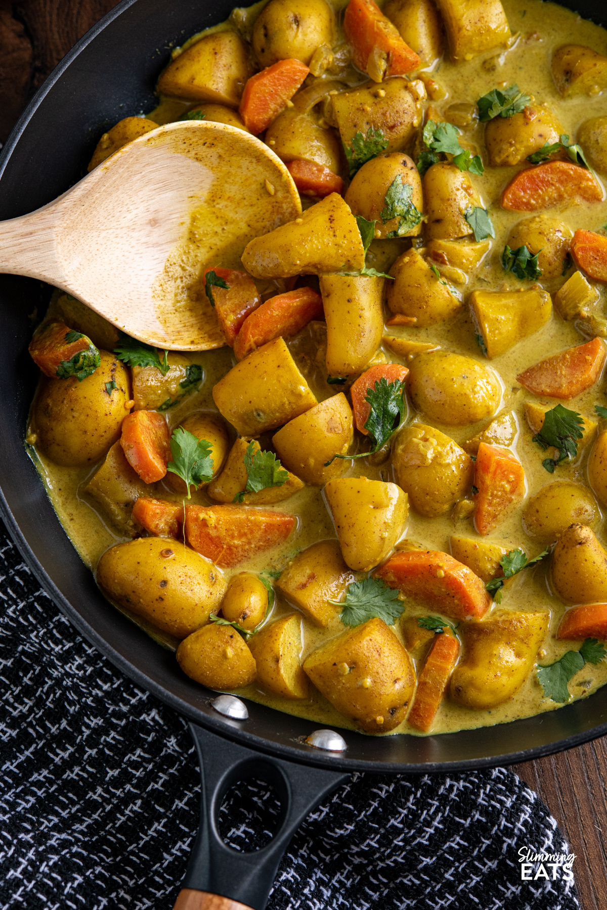 A simple and comforting Creamy Coconut Potato Curry with tender baby potatoes, carrots and warm spices in a rich creamy coconut sauce. close up of Creamy Coconut Potato Curry in a black non stick skillet with wooden handle, with wooden curry spoon in pan