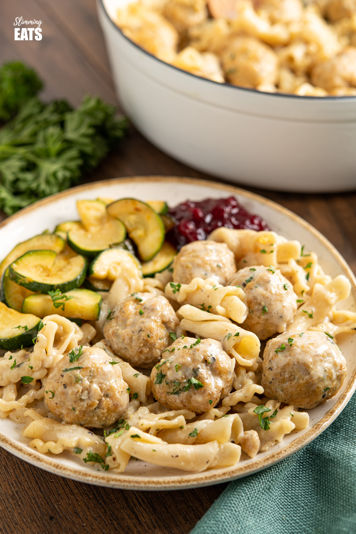 white plate with golden yellow rim dished up with One Pot Turkey Swedish Meatball Pasta sauteed zucchini and lingonberry sauce, pan in background