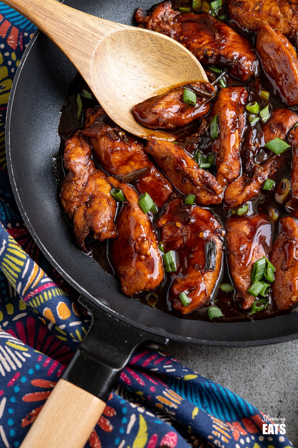 close up of pieces of asian sprite chicken in black frying pan with wooden handle scattered with chopped green onions