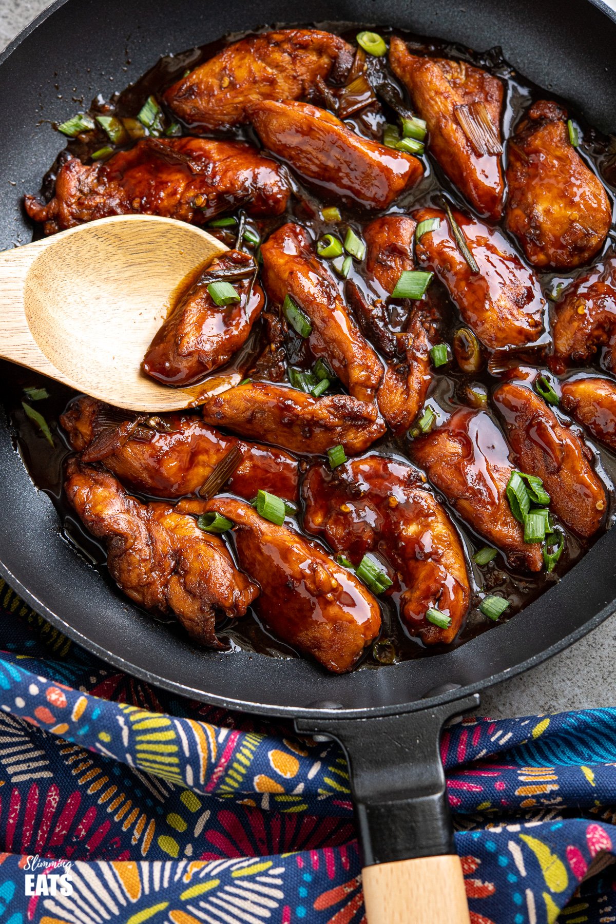 close up of Asian Sprite Chicken in black frying pan with wooden handle, wooden spoon placed in pan