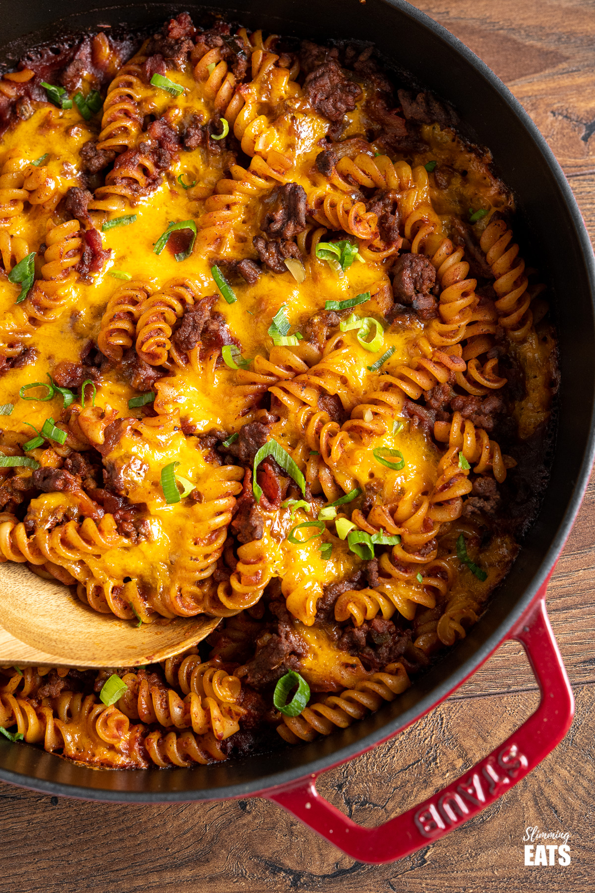 close up of close up of BBQ Bacon Cheeseburger Pasta Bake in red cast iron skillet with wooden spoon