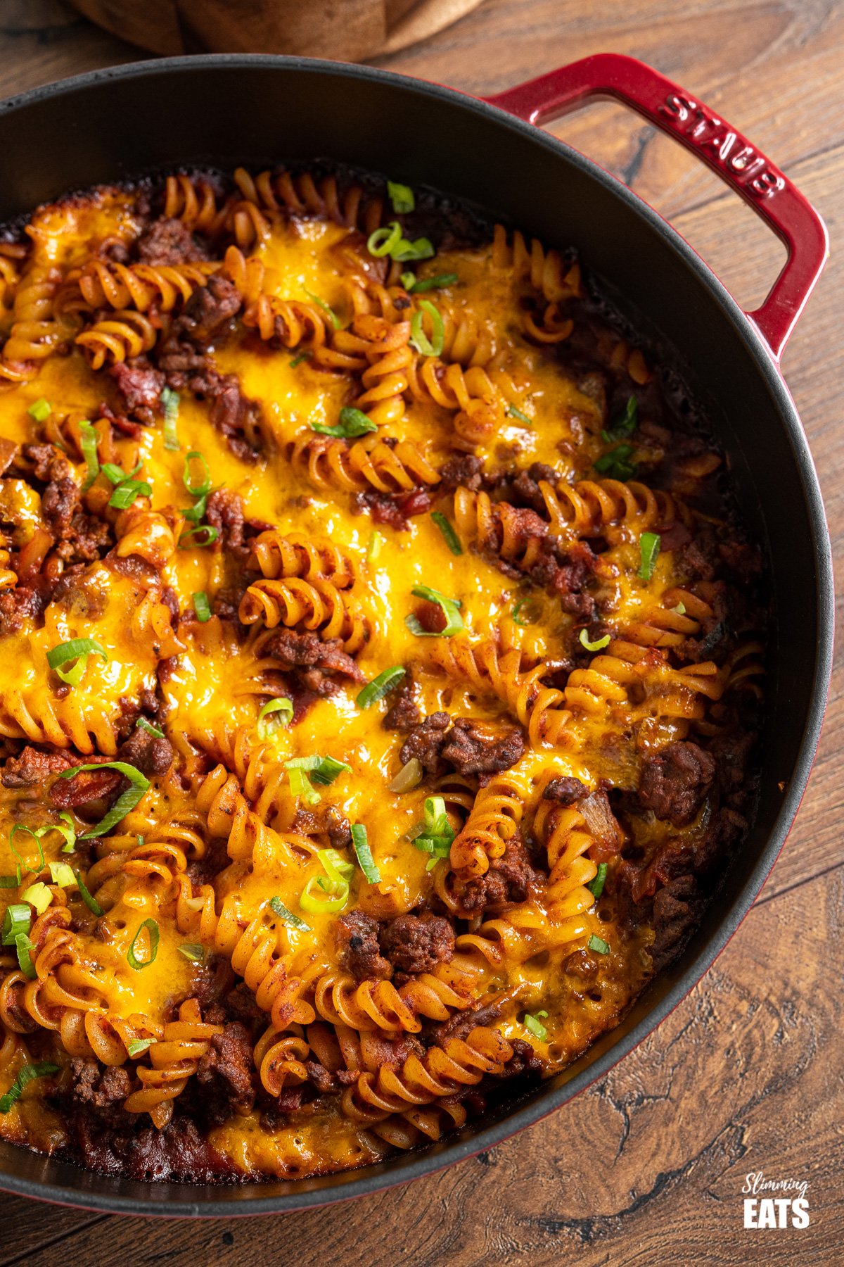 BBQ Bacon Cheeseburger Pasta Bake - ground beef, smokey bacon, a delicious tangy bbq sauce and pasta all topped with gooey melted cheddar cheese. It doesn't get much better than this. Slimming Eats and Weight Watchers friendly close up of BBQ Bacon Cheeseburger Pasta Bake in red cast iron skillet