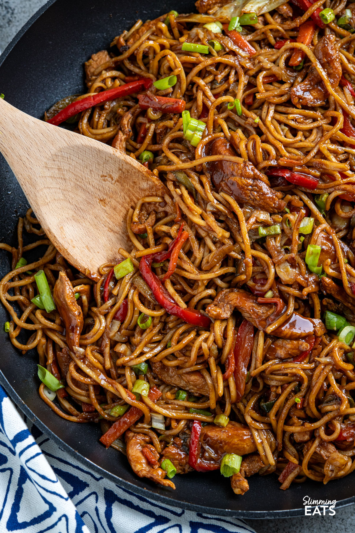 close up of Hoisin Chicken with noodles in black frying pan with wooden spoon