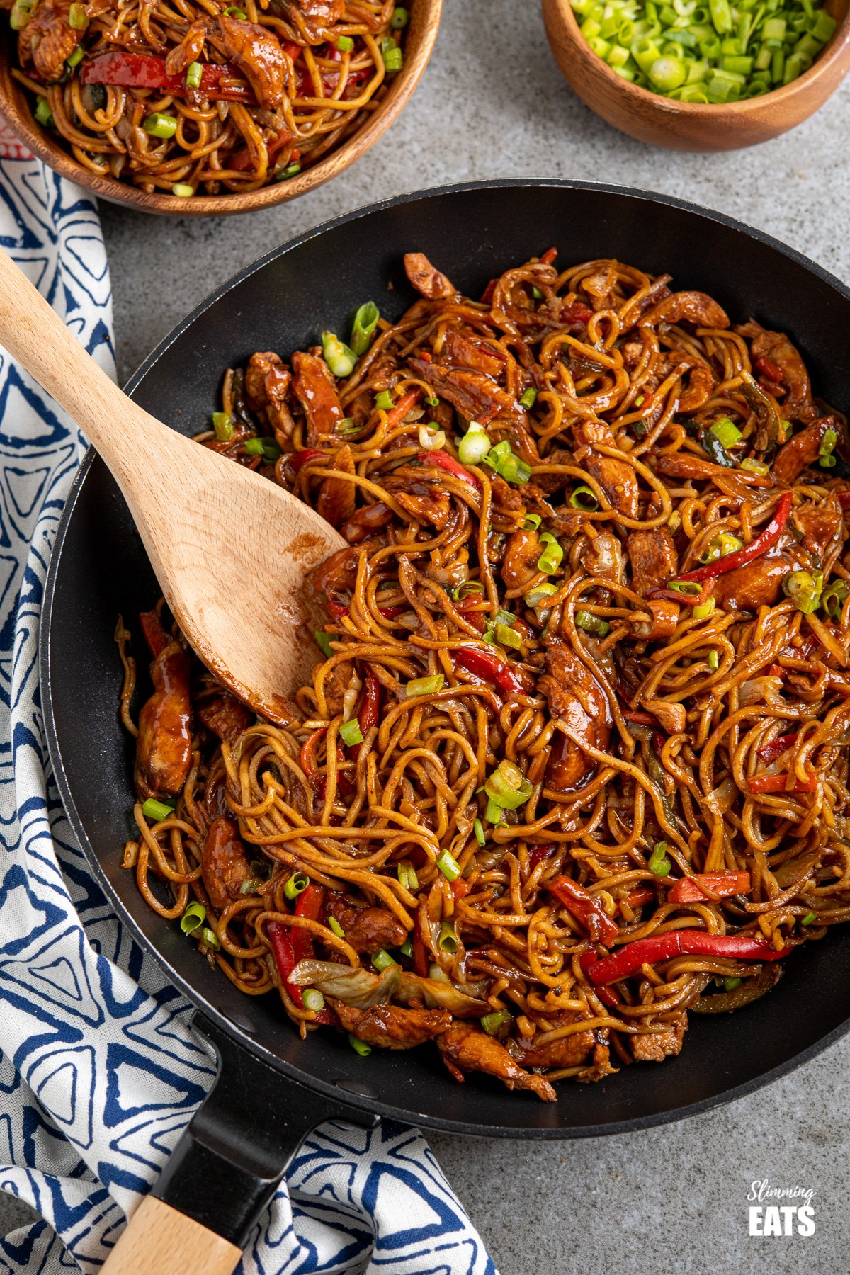  Hoisin chicken noodles in black frying pan with wooden handle, bowl of noodles and spring onions in background