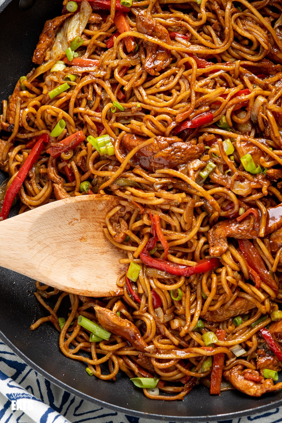 close up of Hoisin Chicken with noodles in black frying pan with wooden spoon