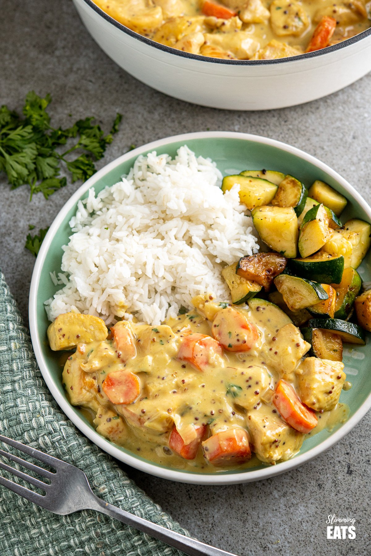 serving of creamy honey mustard chicken with rice and sauteed zucchini on teal plate, pan in background and fork placed to side. 