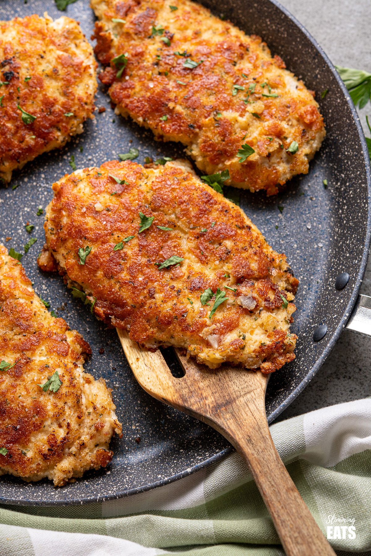 Golden Parmesan Crusted Chicken - tender chicken cutlets coated in parmesan, breadcrumbs, seasoning, and pan-fried until perfectly golden. #slimmingeats #weightwatchers #chicken #parmesan #cutlets Four Golden Parmesan Crusted Chicken cutlets on frying pan with wooden spatual