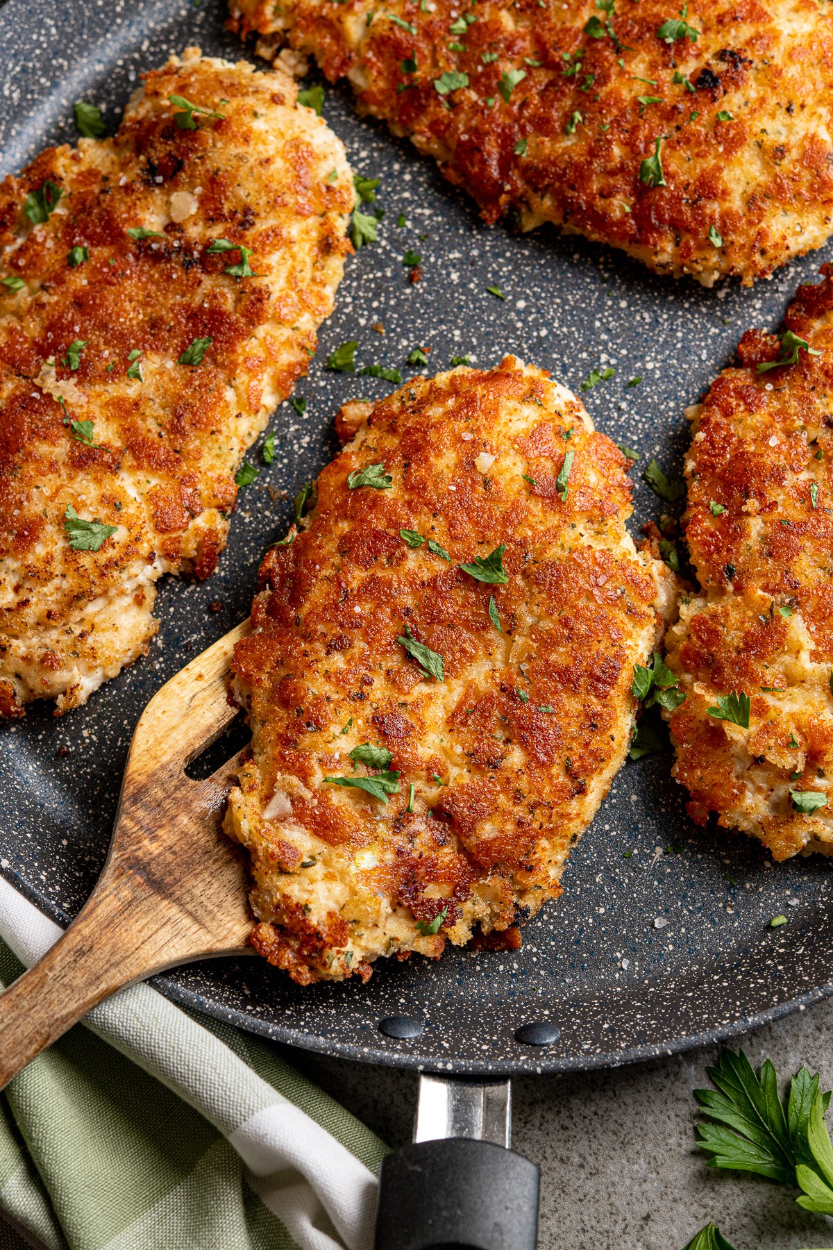 close up of Golden Parmesan Crusted Chicken cutlets on frying pan with wooden spatula