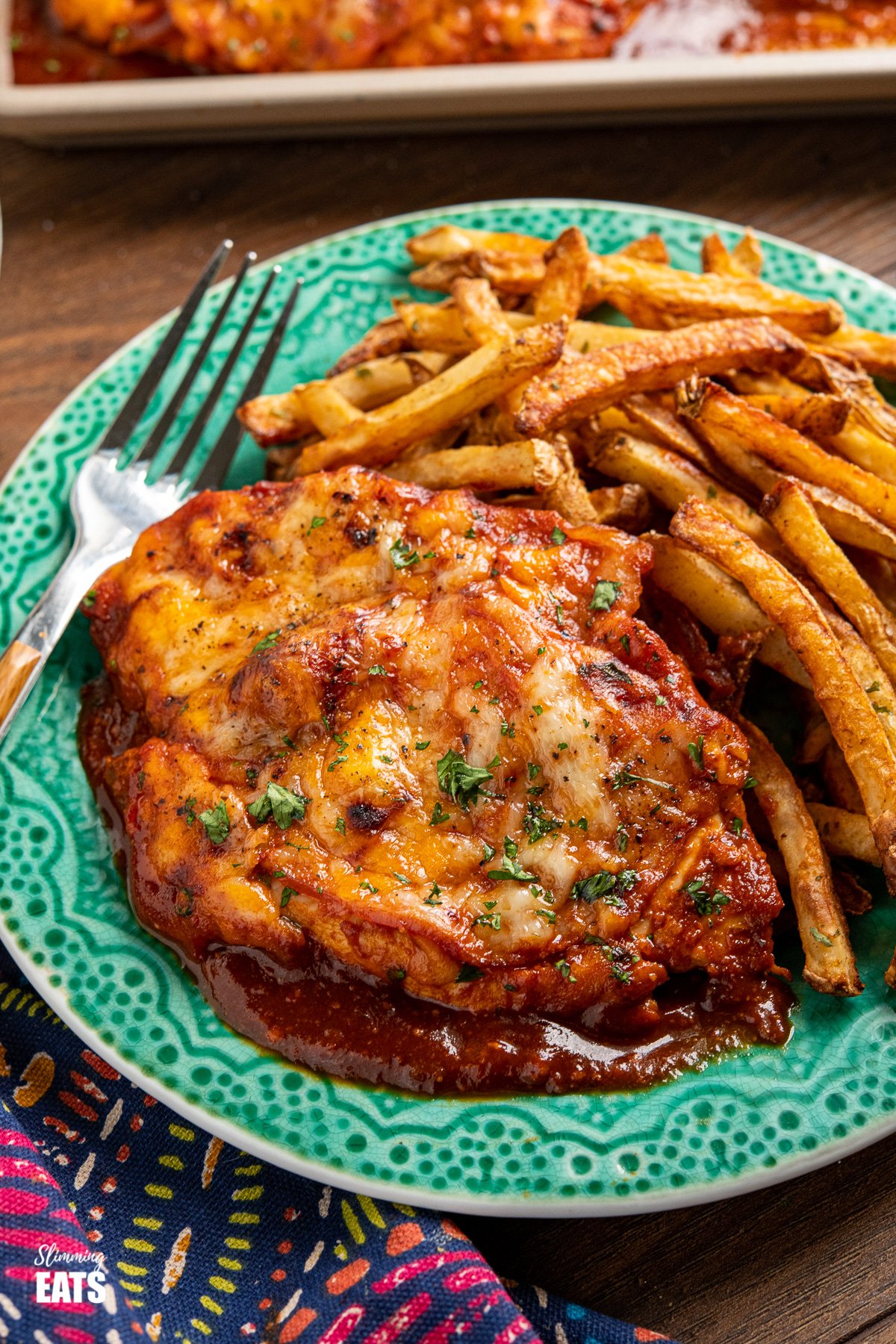Hunters Chicken - tender chicken breasts in a delicious homemade barbecue sauce with slices of smoky bacon, all topped with cheese and baked until melted and golden. #chicken #barbecue #cheese #bacon #slimmingeats #weightwatchers #smartpoints close up of Hunters chicken on teal plate with oven baked fries