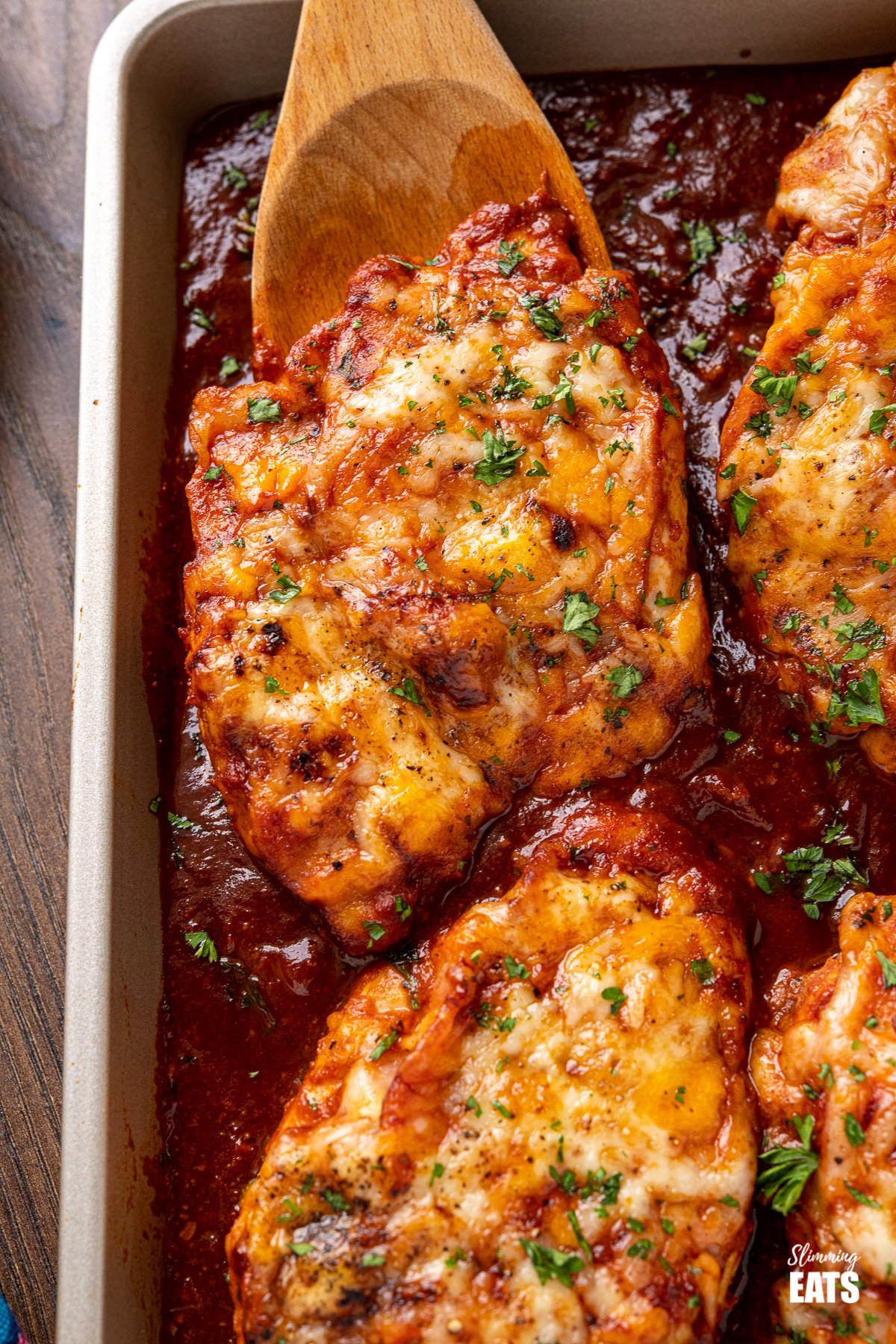 Hunters Chicken - tender chicken breasts in a delicious homemade barbecue sauce with slices of smoky bacon, all topped with cheese and baked until melted and golden. #chicken #barbecue #cheese #bacon #slimmingeats #weightwatchers #smartpoints close up of Hunters Chicken on baking tray with wooden spatula