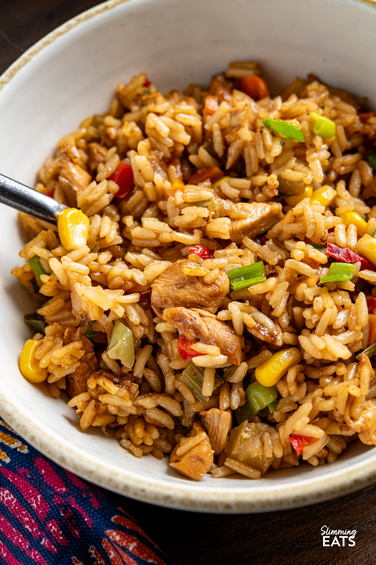 close up of cooked savoury rice with chicken in a white bowl with beige rim