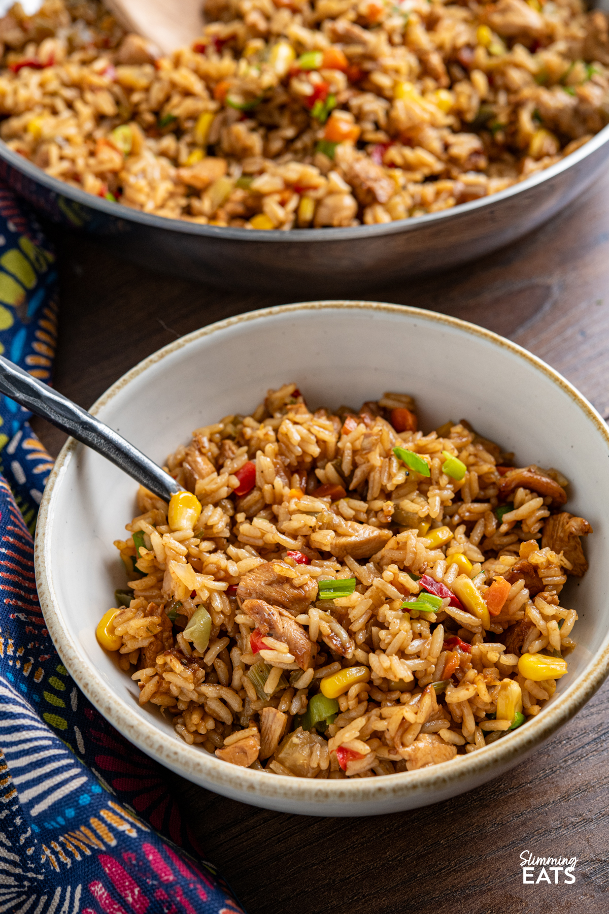 cooked savoury rice with chicken in a white bowl with beige rim next to stainless steel pan filled with the rice