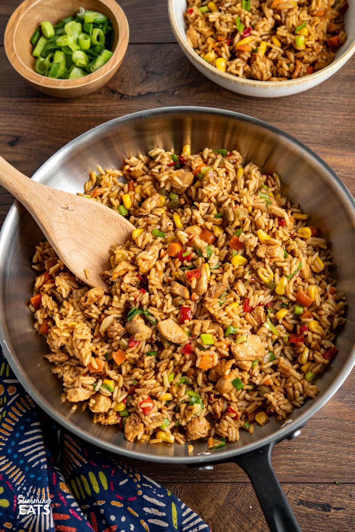 cooked savoury rice with chicken in a black handled stainless steel pan with wooden spoon
