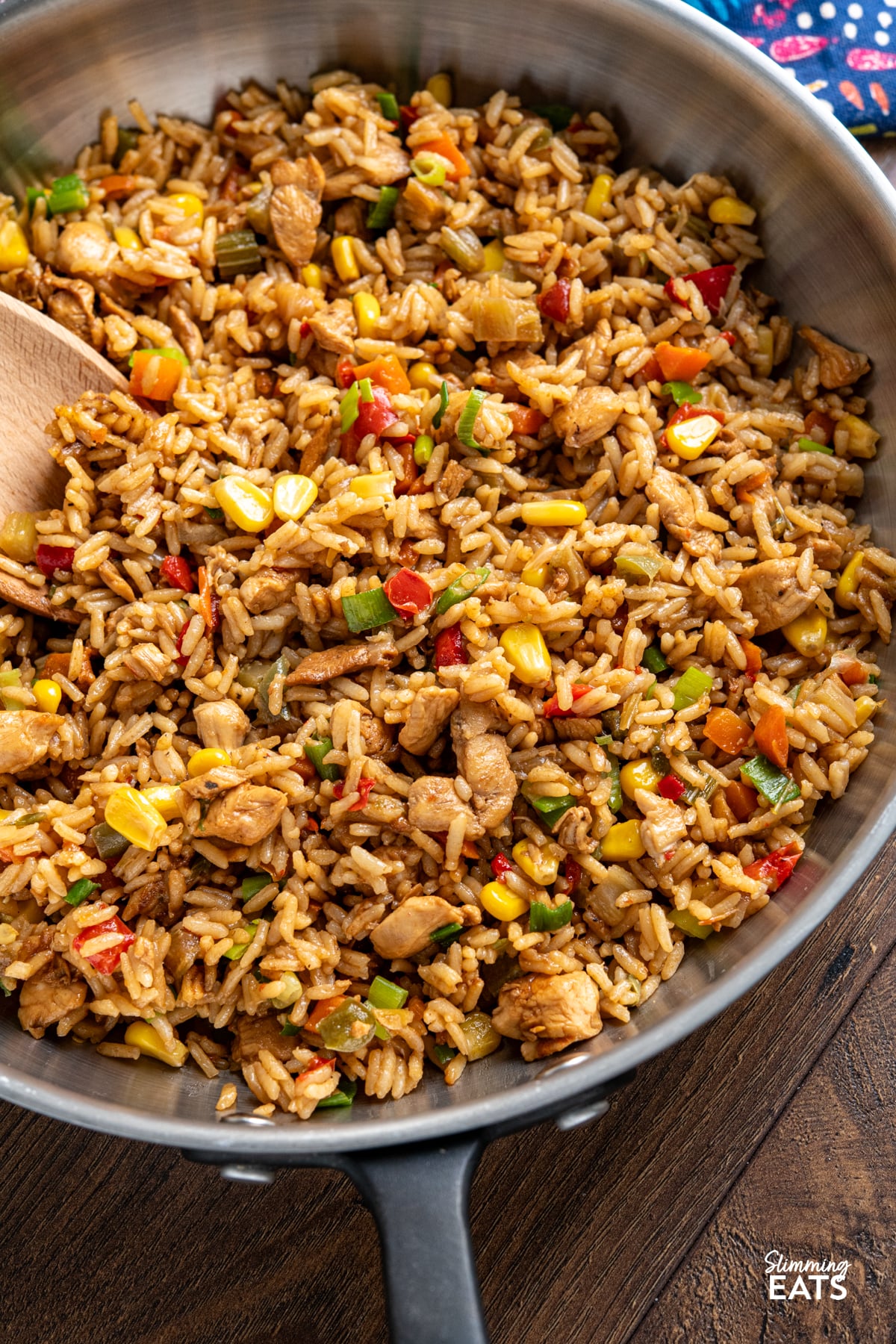 close up of cooked savoury rice with chicken in a black handled stainless steel pan with wooden spoon
