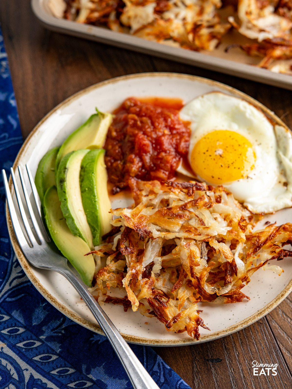 sheet pan hash browns cooked on plate with sunny side egg, salsa and avocado.