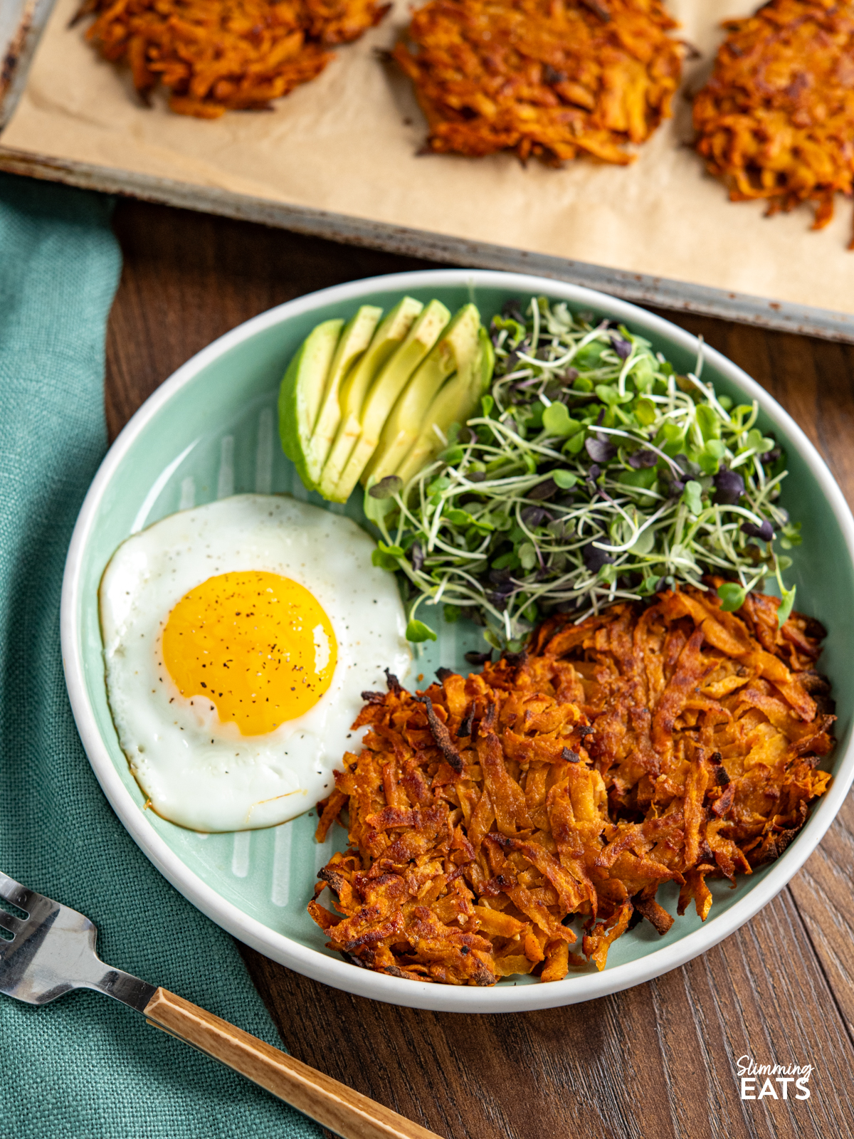 sweet potato hash browns all cooked on a light jade green plate with sunny side up egg, micro greens and half an avocado sliced. 