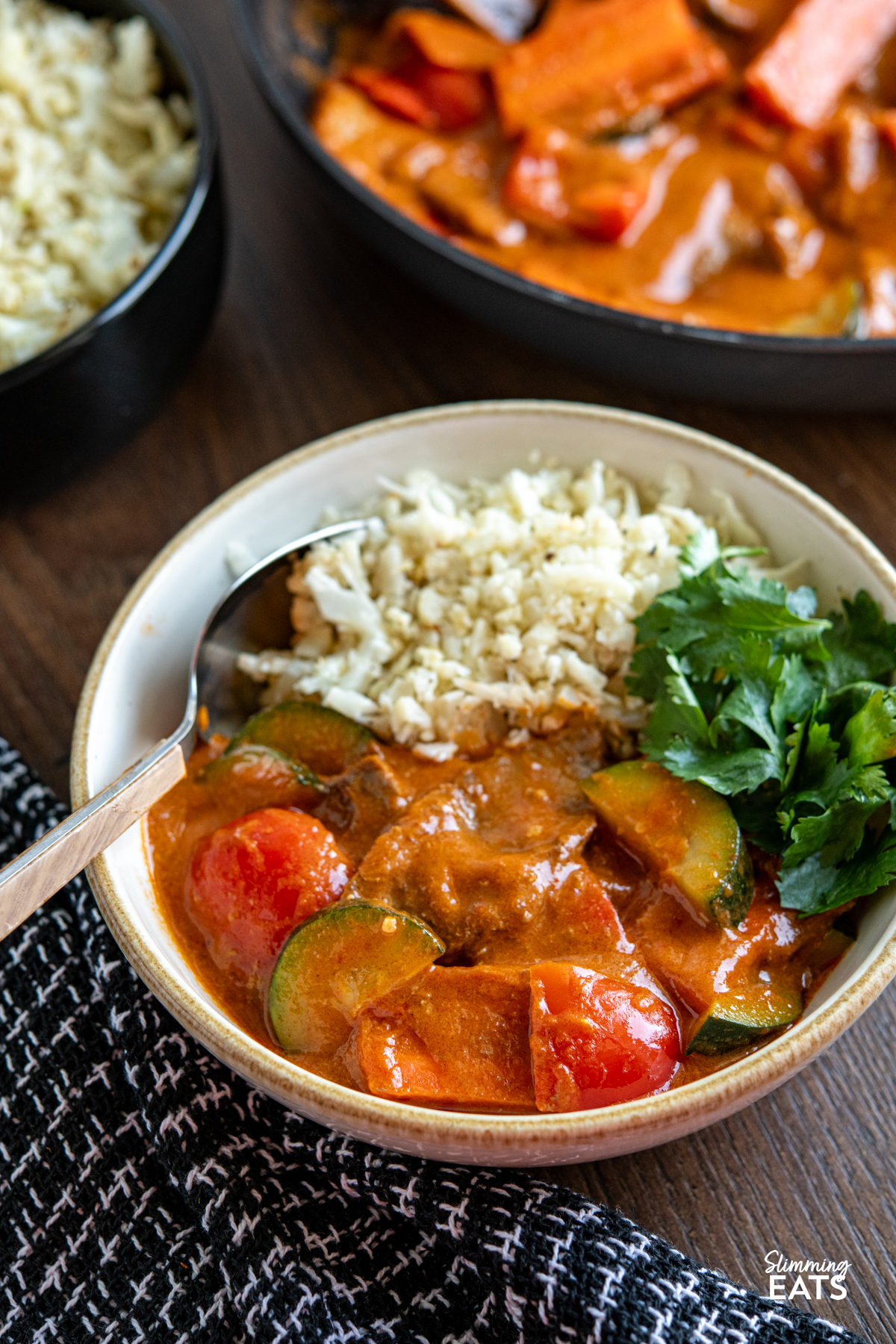 thai red beef curry in white bowl with cauliflower rice, frying pan of curry in background