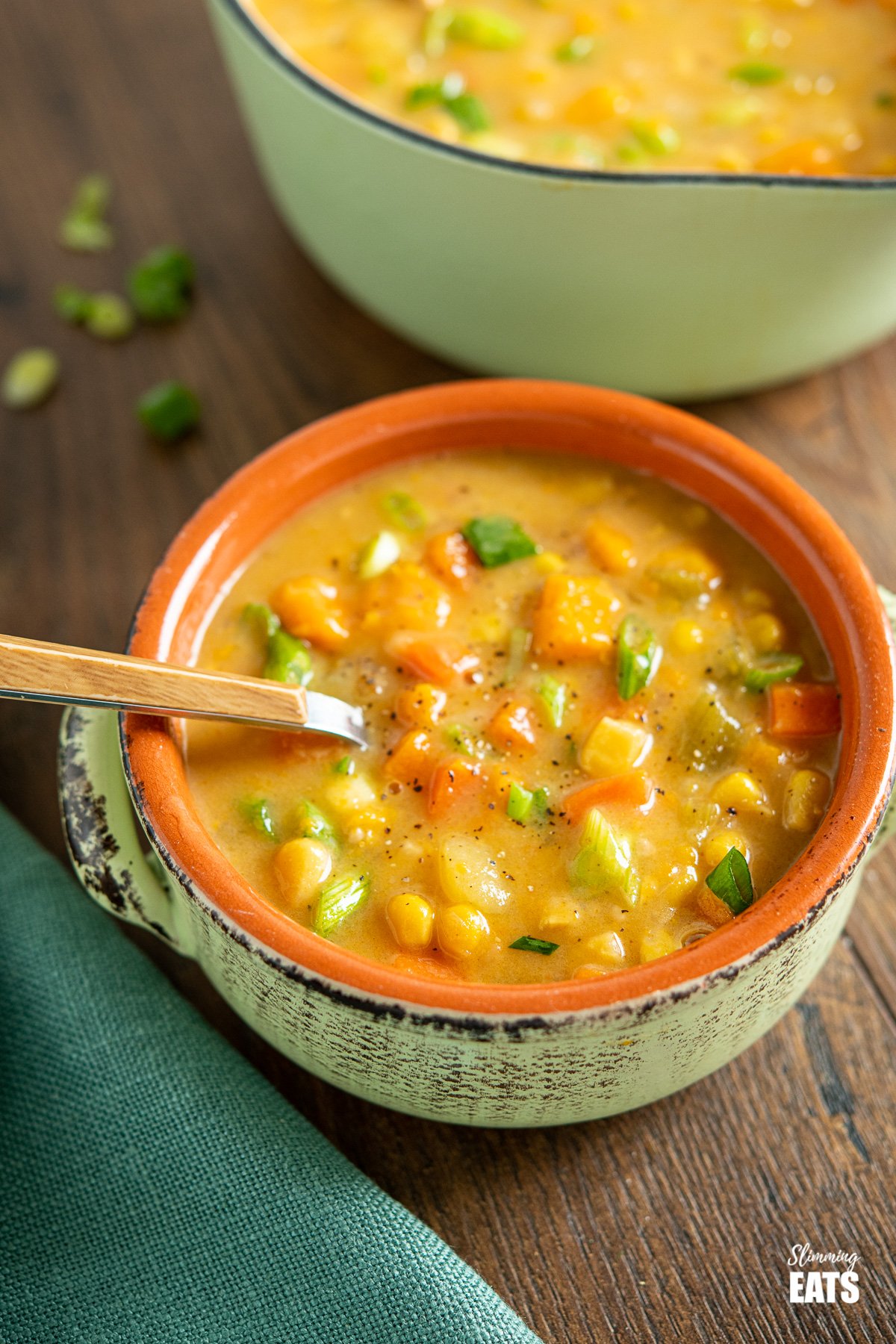 serving on creamy vegan vegetable chowder in ceramic bowl on wooden board, saucepan of soup in background