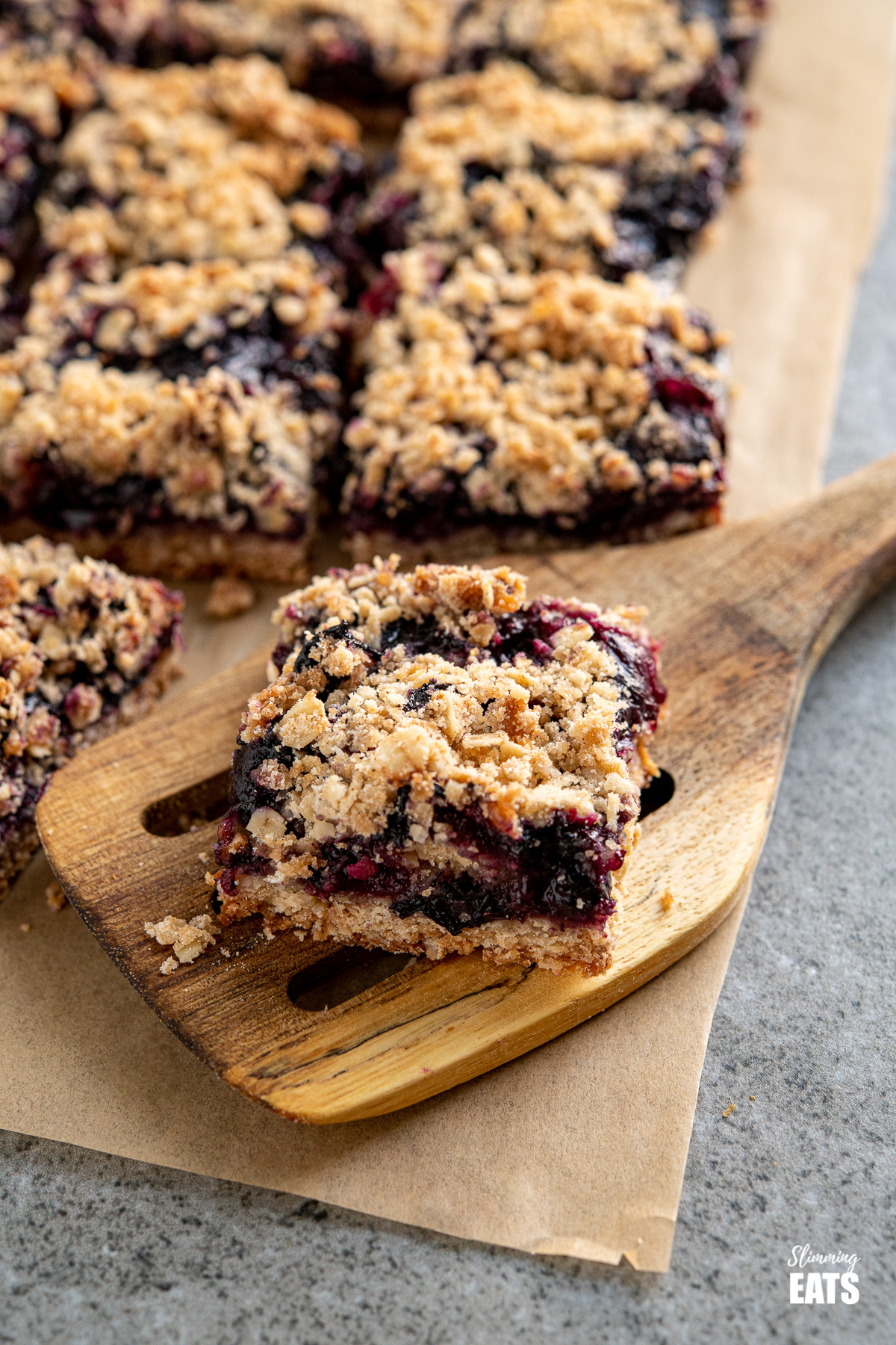 sliced blueberry oat crumble bars on parchment paper, one placed on a spatula
