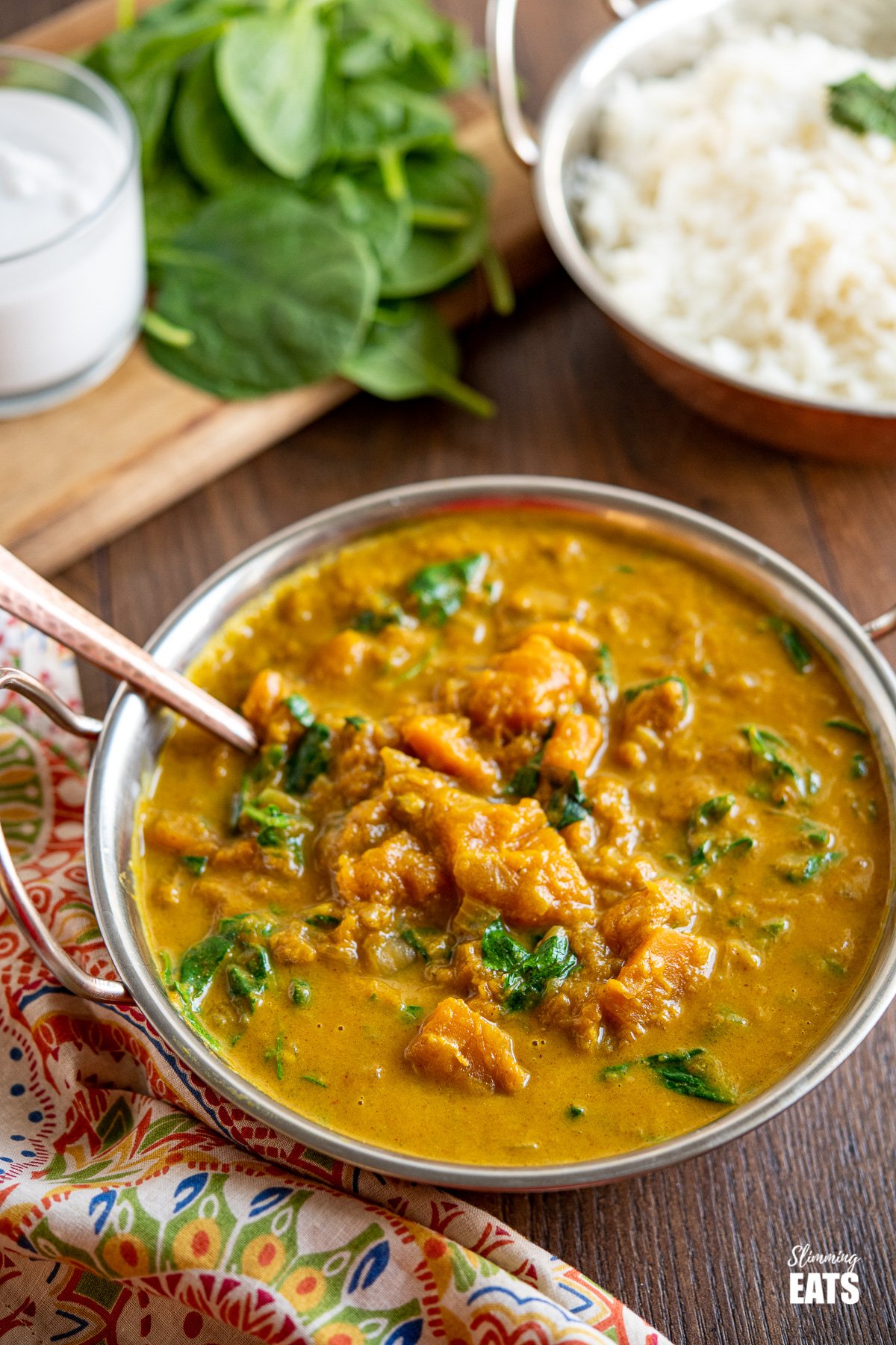 Easy Butternut Squash Curry with Spinach in metal dish with bowl of rice, spinach and coconut milk in the background