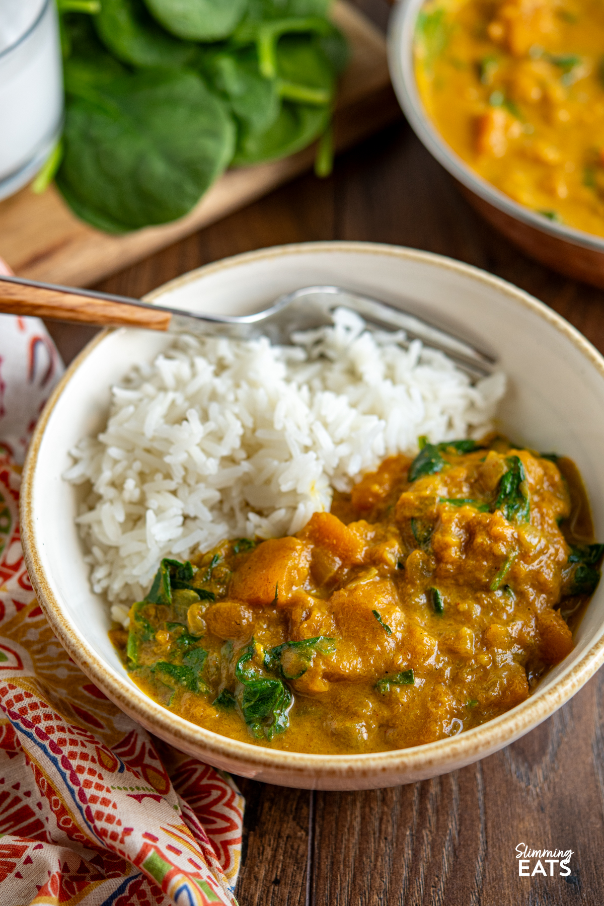 Easy Butternut Squash Curry with Spinach - a simple delicious vegan curry with chunks of butternut squash and a creamy coconut curry sauce. It's a perfect recipe for the whole family. #vegan #vegetarian #butternutsquash #curry #coconut #slimmingeats #weightwatchers Easy Butternut Squash Curry with Spinach in a white bowl with rice, spinach and curry dish in background