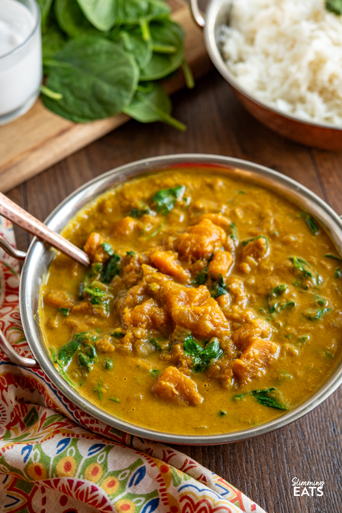 Easy Butternut Squash Curry with Spinach - a simple delicious vegan curry with chunks of butternut squash and a creamy coconut curry sauce. It's a perfect recipe for the whole family. #vegan #vegetarian #butternutsquash #curry #coconut #slimmingeats #weightwatchers Easy Butternut Squash Curry with Spinach in metal dish with bowl of rice, spinach and coconut milk in the background