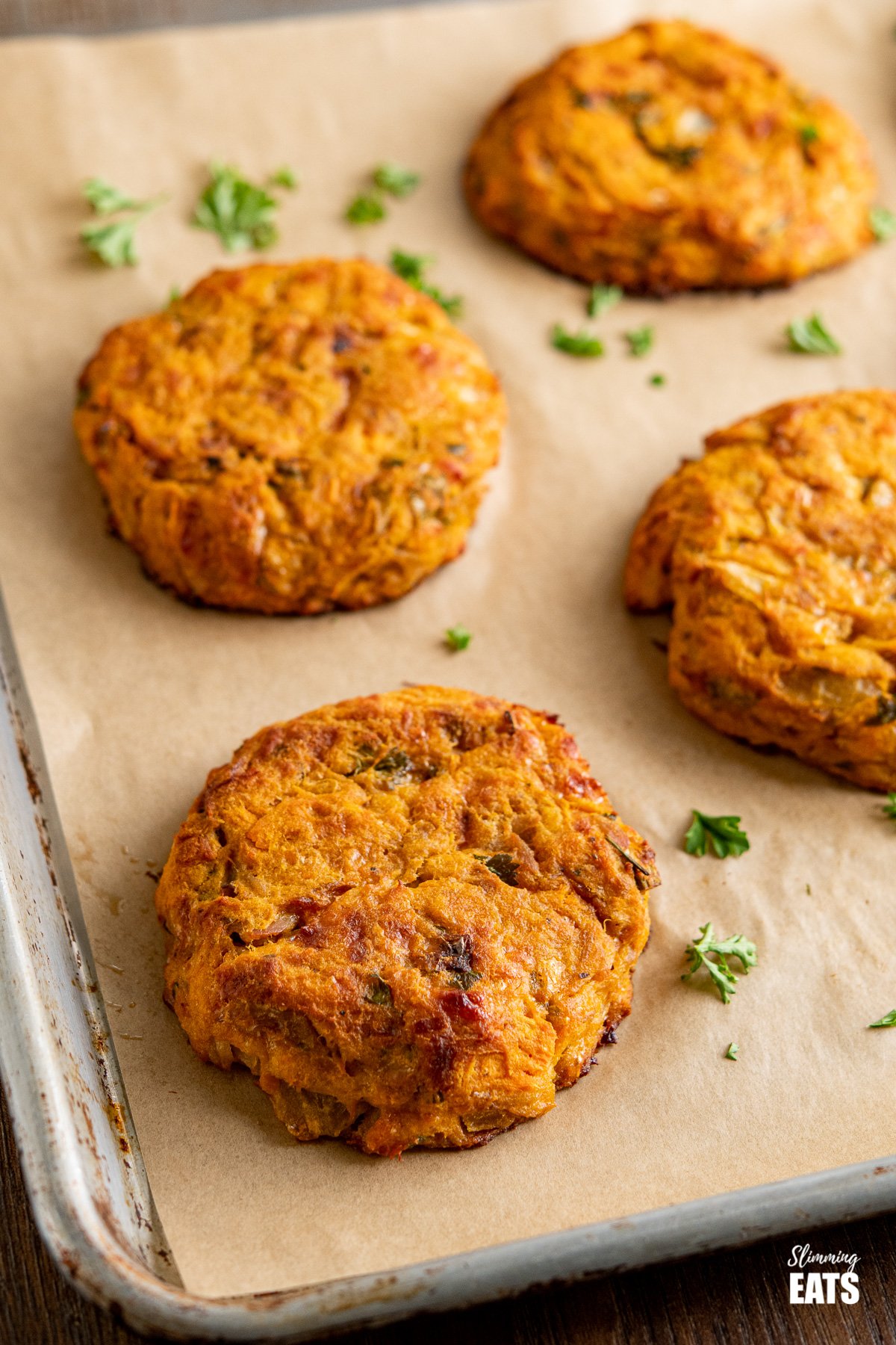 Tuna Sweet Potato Cheddar Patties on parchment lined baking tray with scattered parsley