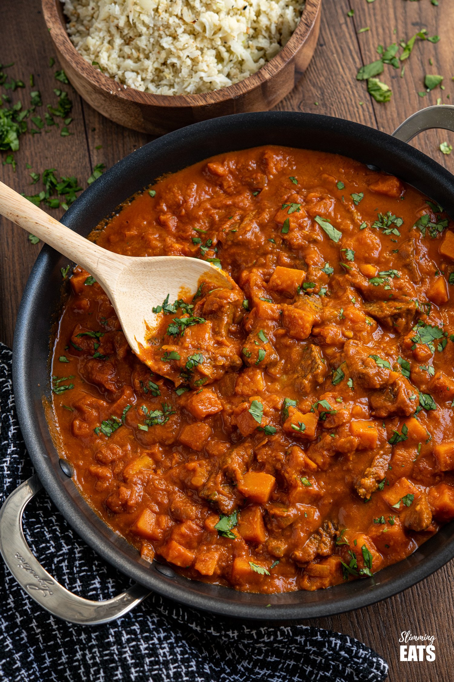 Beef and Sweet Potato Tikka Masala in a black pan with wooden spoon and roasted cauliflower rice in a wooden bowl