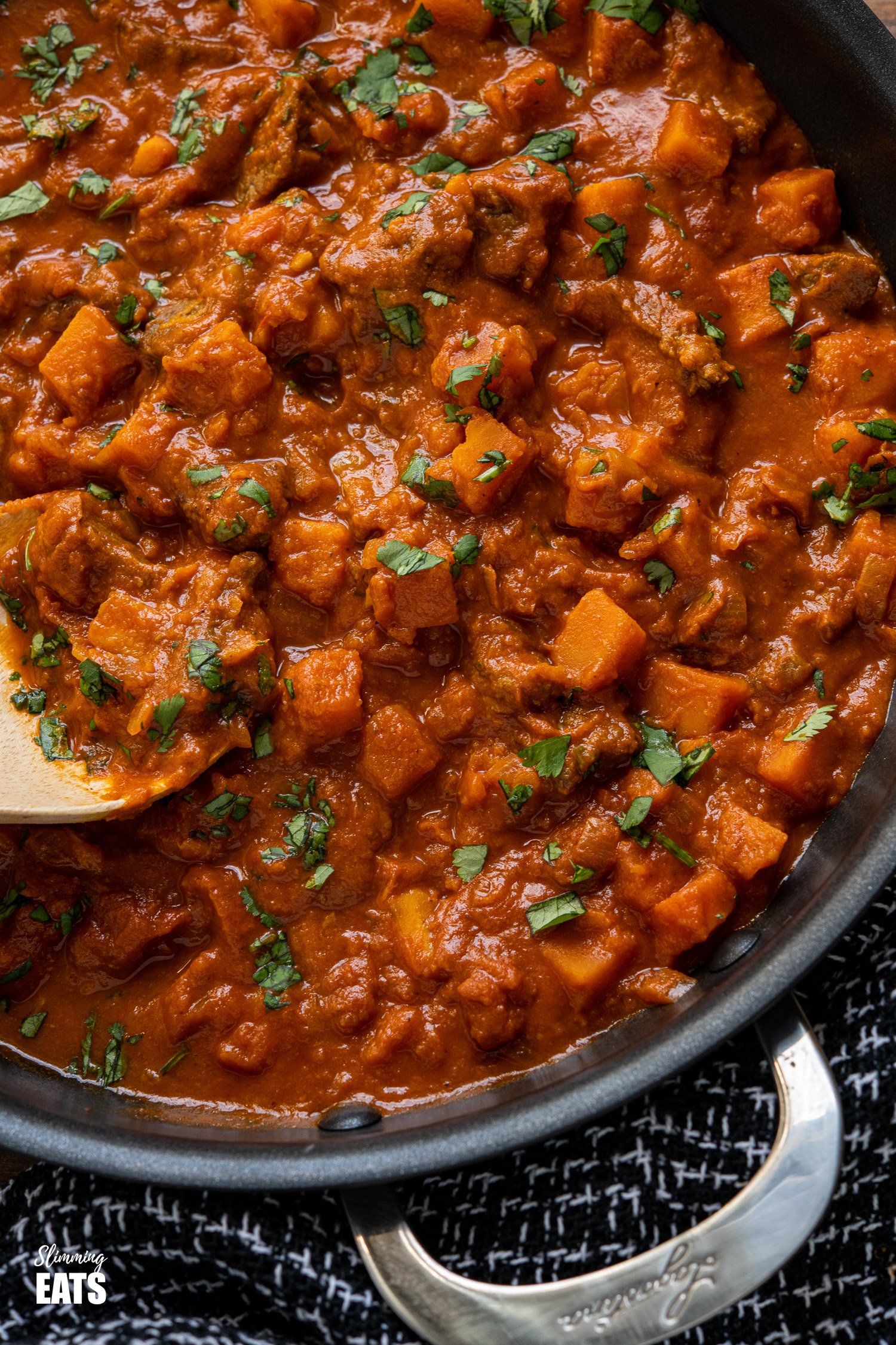 close up of Beef and Sweet Potato Tikka Masala in a black pan with wooden spoon