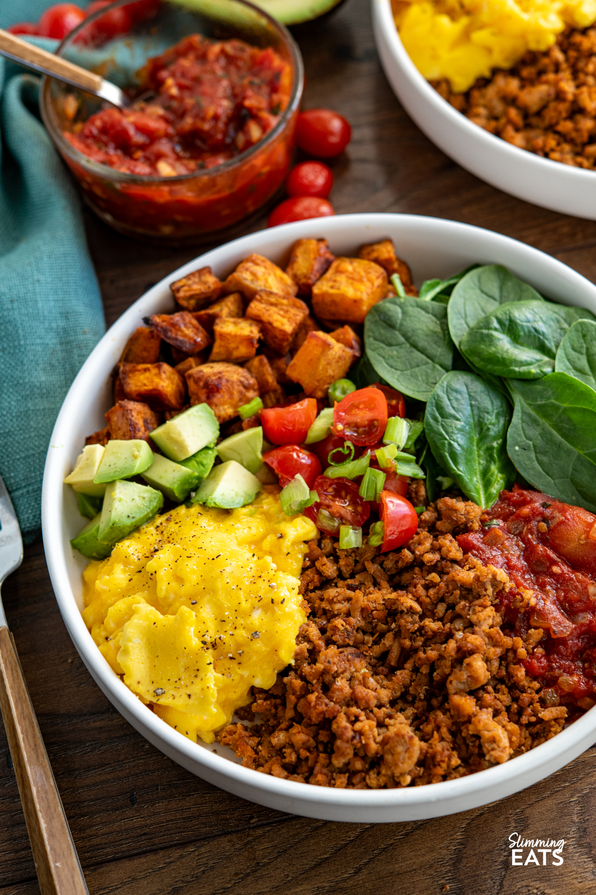 Taco Breakfast Bowl - lean seasoned ground turkey with sweet potato, spicy tomatoes, spinach, avocado and perfectly scrambled eggs for a filling high protein start to the day. #slimmingeats #weightwatchers #taco #breakfast #eggs #glutenfree #dairyfree #paleo #whole30 turkey taco meat, eggs, spinach, sweet potato, avocado, tomatoes in a bowl with additional bowl in background with scattered tomatoes and half an avocado