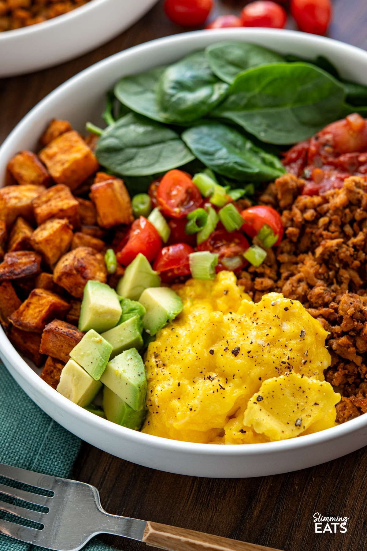 Taco Breakfast Bowl - lean seasoned ground turkey with sweet potato, spicy tomatoes, spinach, avocado and perfectly scrambled eggs for a filling high protein start to the day. #slimmingeats #weightwatchers #taco #breakfast #eggs #glutenfree #dairyfree #paleo #whole30 turkey taco meat, eggs, spinach, sweet potato, avocado, tomatoes in a bowl with additional bowl in background with scattered tomatoes and half an avocado