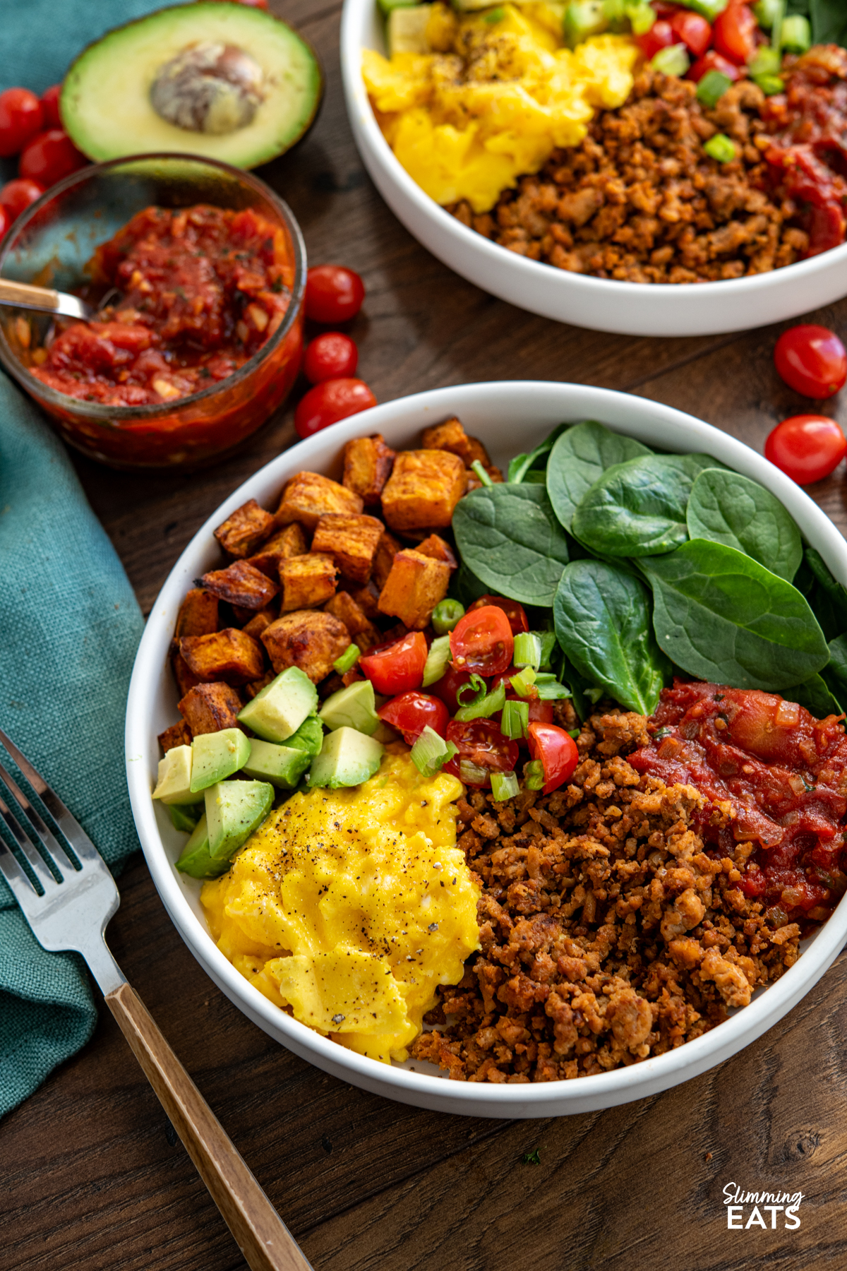 Taco Breakfast Bowl - lean seasoned ground turkey with sweet potato, spicy tomatoes, spinach, avocado and perfectly scrambled eggs for a filling high protein start to the day. #slimmingeats #weightwatchers #taco #breakfast #eggs #glutenfree #dairyfree #paleo #whole30 turkey taco meat, eggs, spinach, sweet potato, avocado, tomatoes in a bowl with additional bowl in background with scattered tomatoes and half an avocado