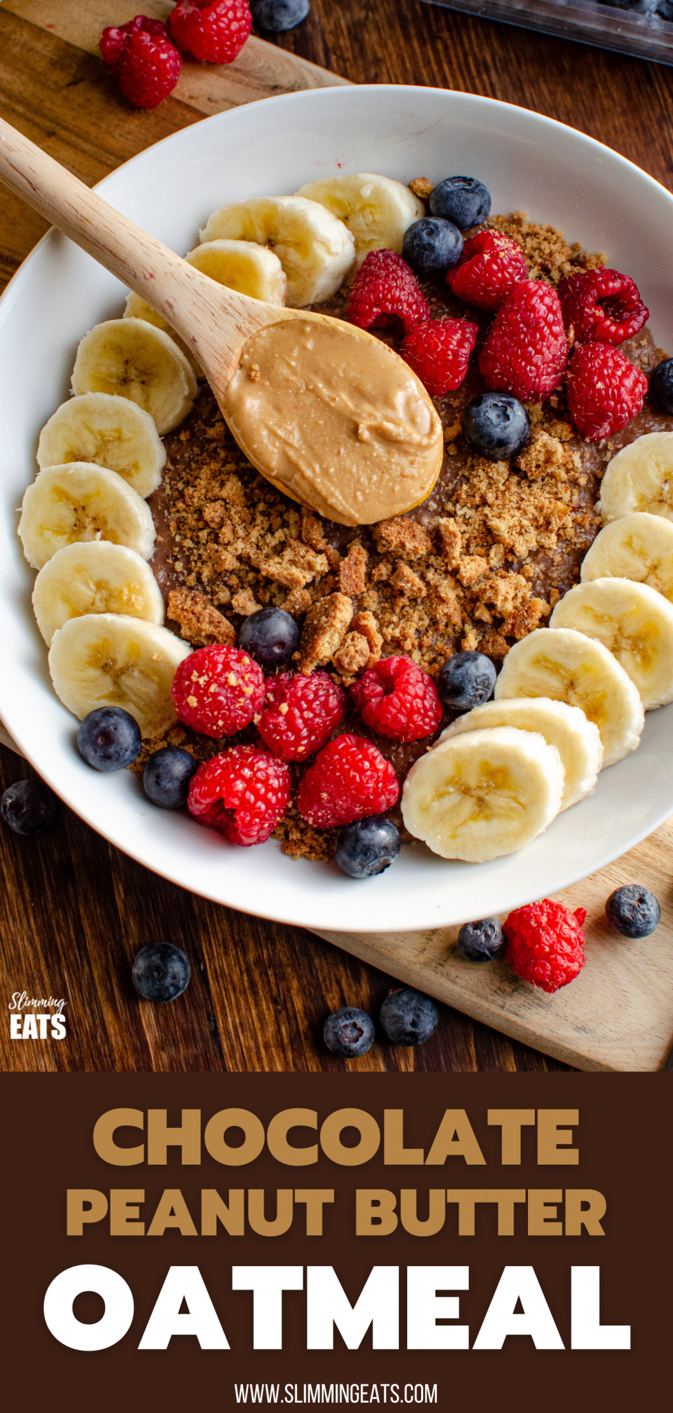 Chocolate Peanut Butter Oatmeal in white bowl with wooden spoon of peanut butter, slices of banana, raspberries, blueberries and a mini crumbled cookie