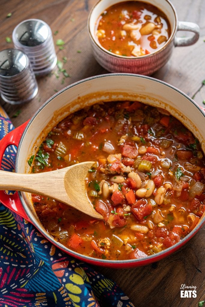 chicken, tomato and white bean soup in a cerise cast iron pot with mug of soup in background and salt and pepper shakers