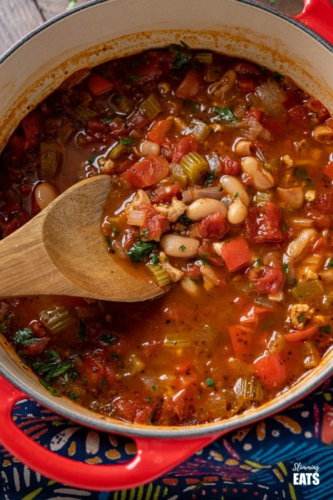 Chicken, Tomato and White Bean Soup - this hearty flavoursome soup is a complete meal in a bowl that the whole family will love. Gluten Free, Slimming World and Weight Watchers friendly close up of Chicken, Tomato and White Bean Soup in cerise cast iron pot